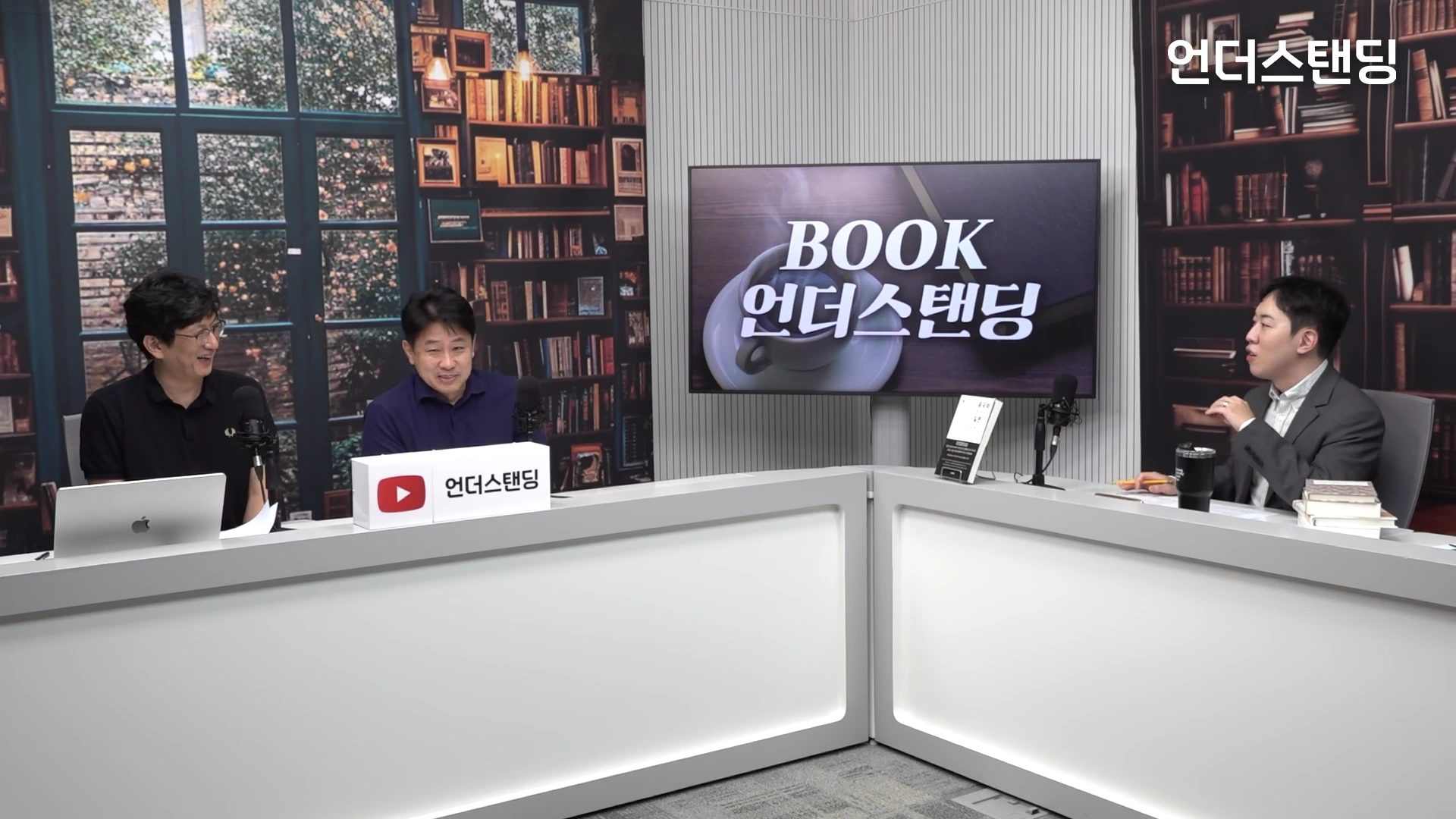 서재 배경의 스튜디오에서 세 명의 남자가 책상 앞에 앉아 대화를 나누고 있는 모습. 가운데 테이블에는 '언더스탠딩' 로고가 적힌 상자가 있고, 뒤쪽 스크린에는 프로그램 로고가 떠 있다.