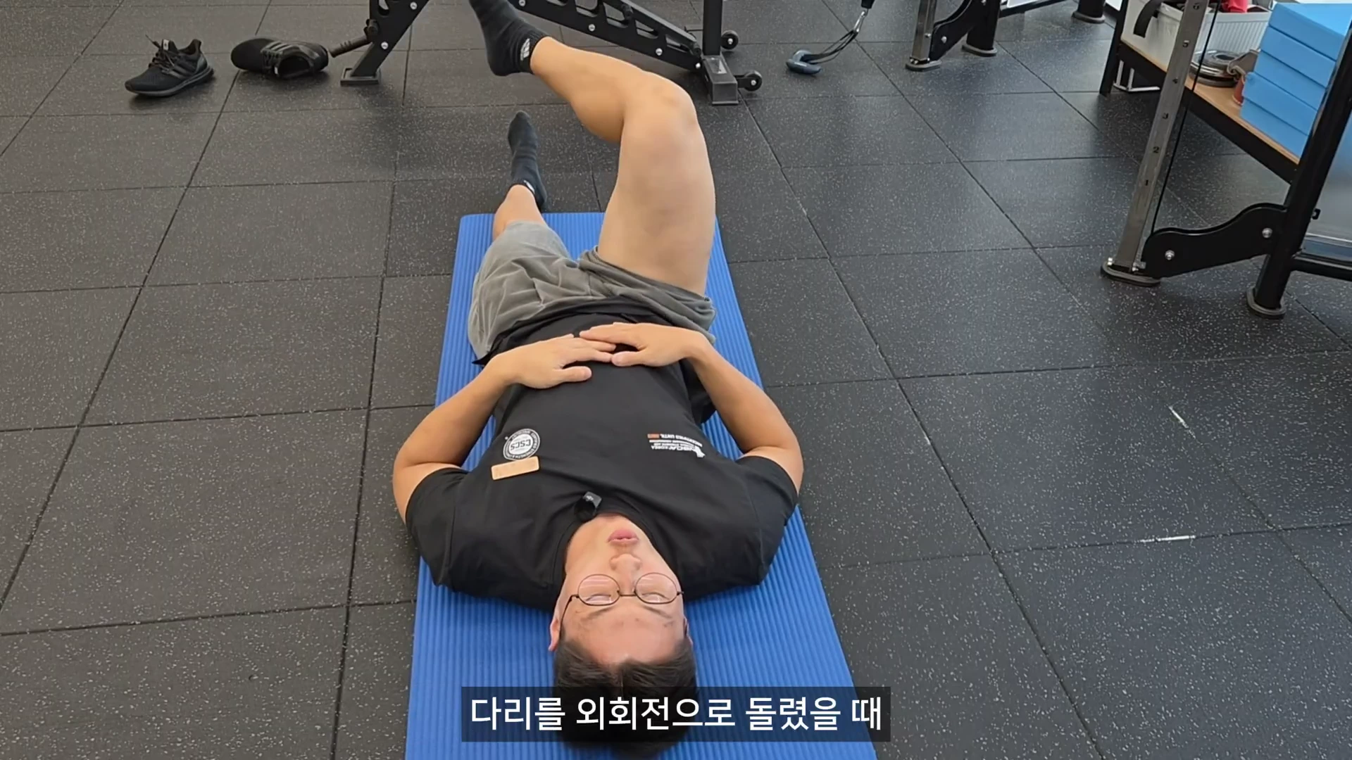 운동복을 입은 남성이 매트 위에 누워 한쪽 다리를 들어 올린 채 외회전 동작을 수행하고 있는 모습