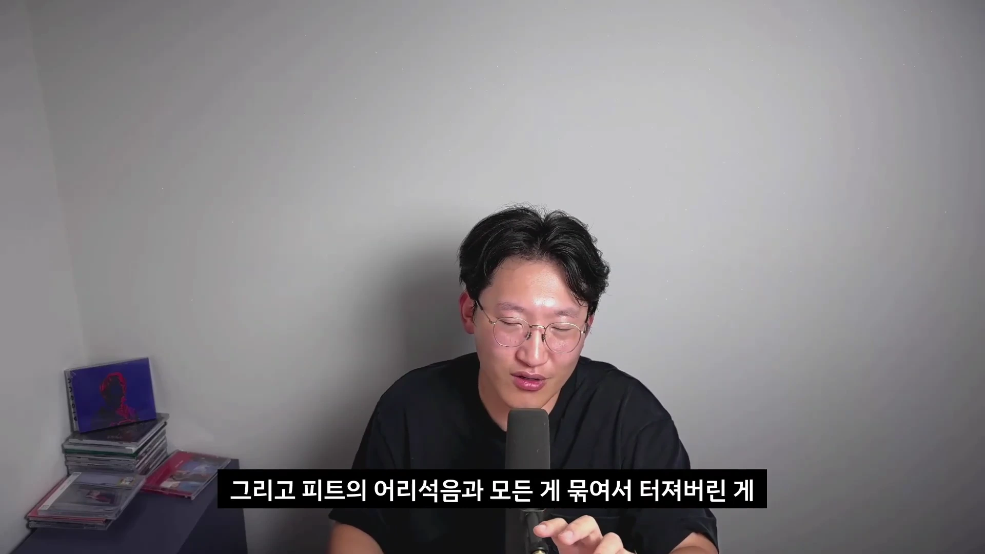 안경을 쓴 남성이 마이크 앞에서 이야기하고 있으며 하단에 '그리고 피트의 어리석음과 모든 게 묶여서 터져버린 게'라는 자막이 표시되어 있다.