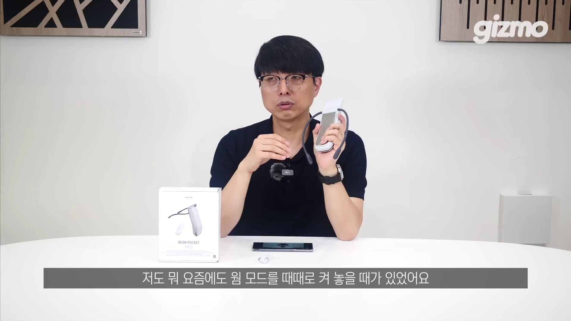 안경을 쓴 남성이 흰색 테이블에 앉아 소니 휴대용 냉온풍기 본체와 제품 상자를 손에 들고 설명하는 모습