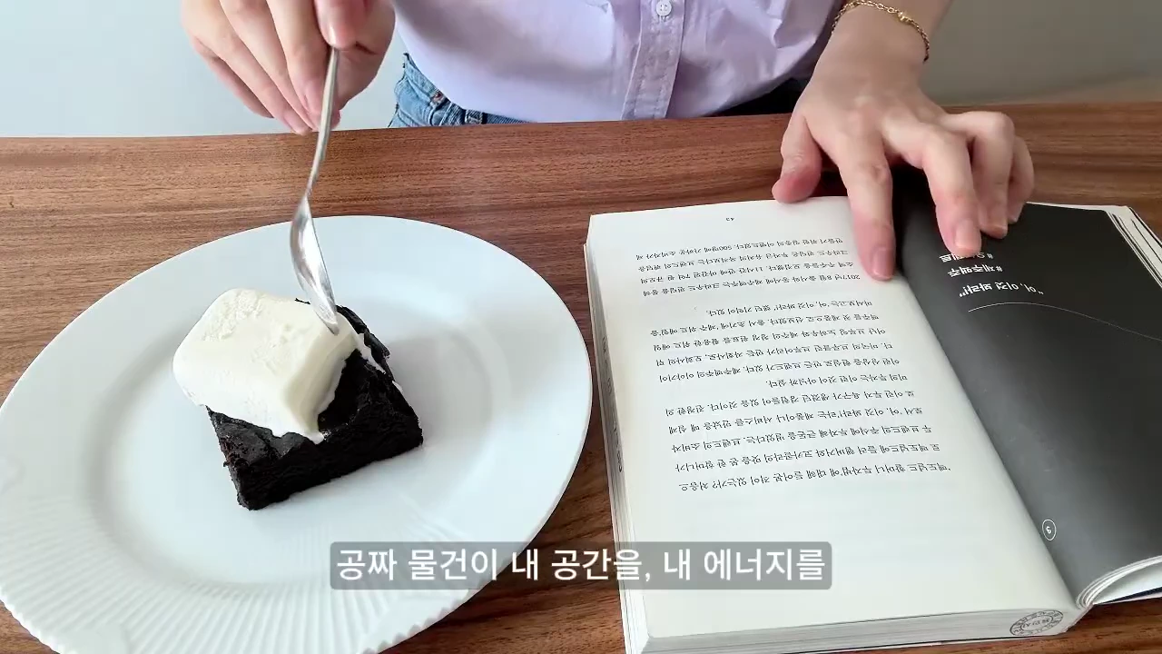 테이블 위에 아이스크림이 올라간 브라우니 접시와 책이 펼쳐져 있고, 한 사람이 숟가락을 들고 있는 모습.