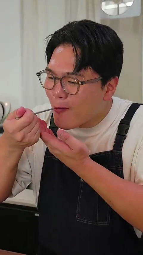 안경을 쓴 남성이 숟가락으로 음식을 떠서 입으로 가져가 맛을 보고 있는 모습