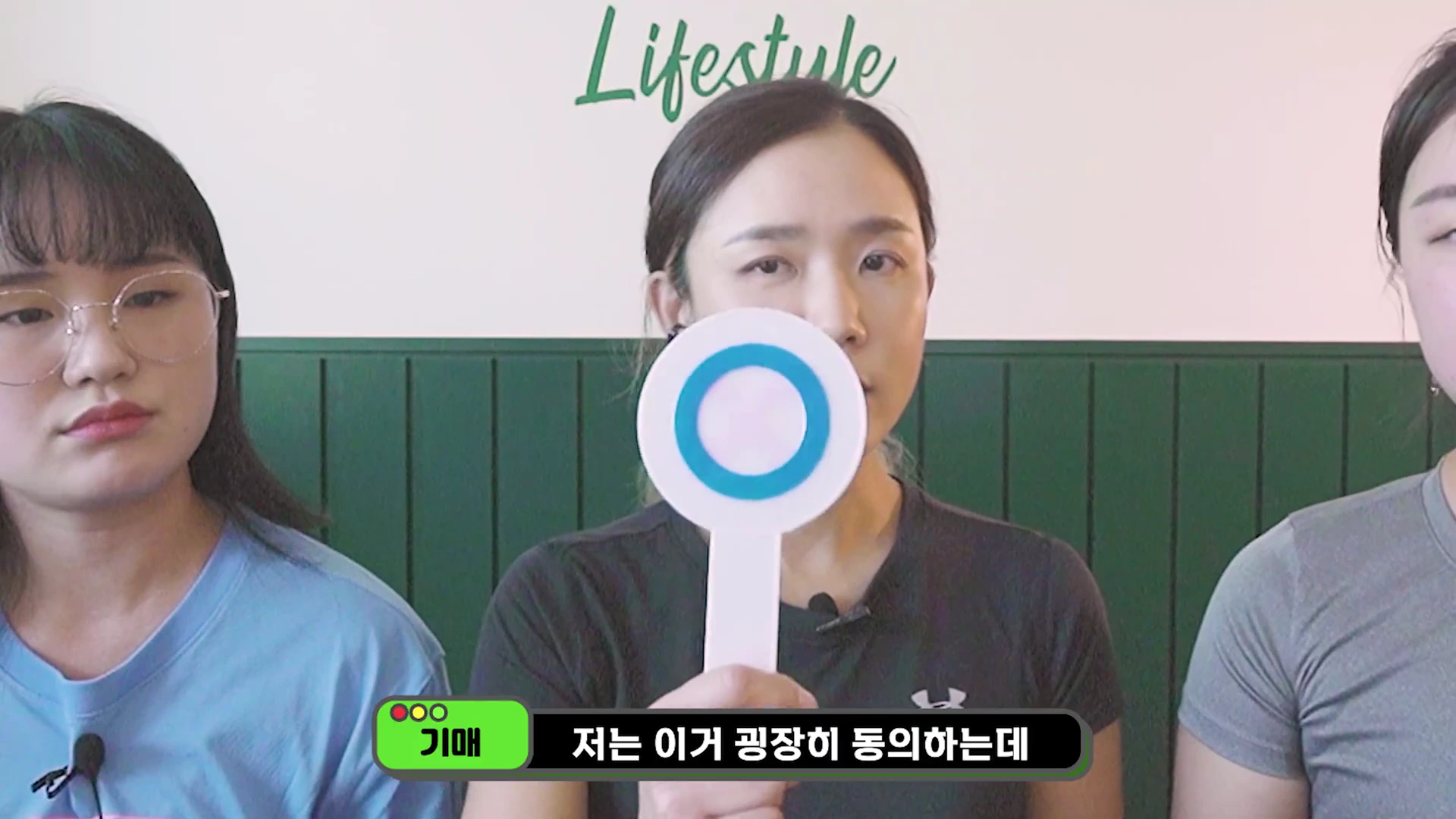 세 명의 여성이 앉아 있는 모습으로, 가운데에 있는 여성이 파란색 원이 그려진 O 모양의 팻말을 들어 보이고 있으며 하단에 출연자 이름과 자막이 표시되어 있습니다.