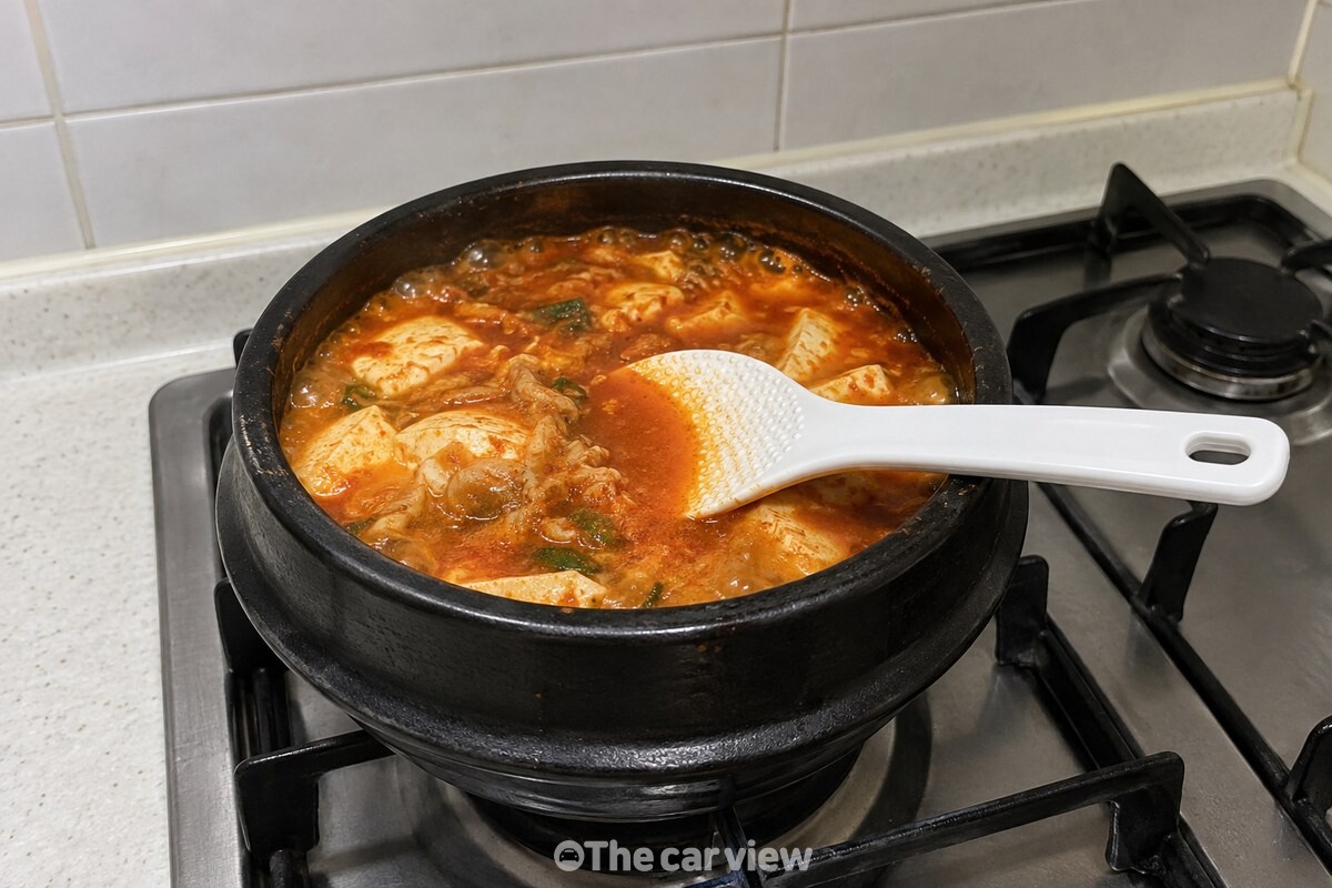 뚝배기에 순두부와 붉은 국물이 담긴 순두부찌개에 흰 플라스틱 주걱이 놓여 있다. / 기사 이해를 돕기 위한 생성형 이미지