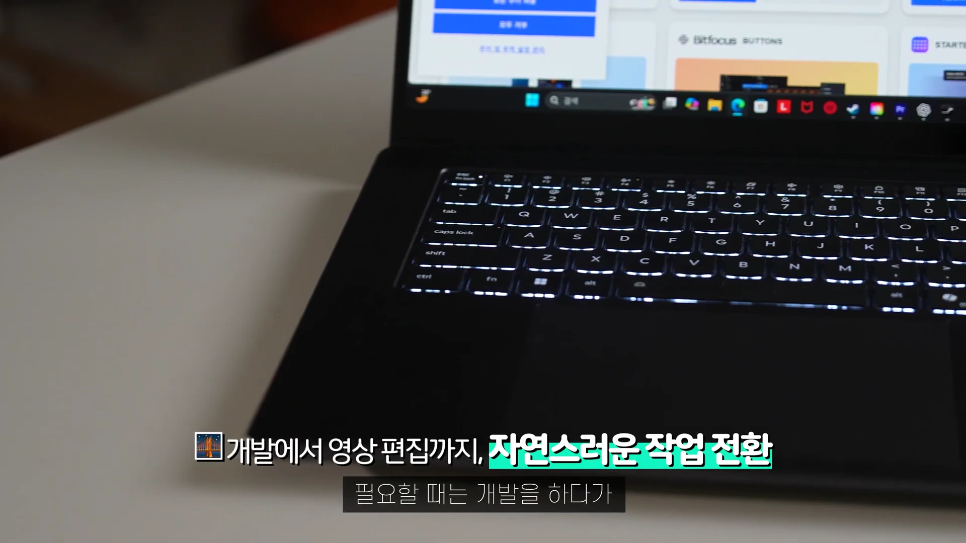 흰색 책상 위에 놓인 어두운 색 노트북의 키보드와 화면 하단부, 화면에 표시된 작업 환경이 클로즈업된 모습