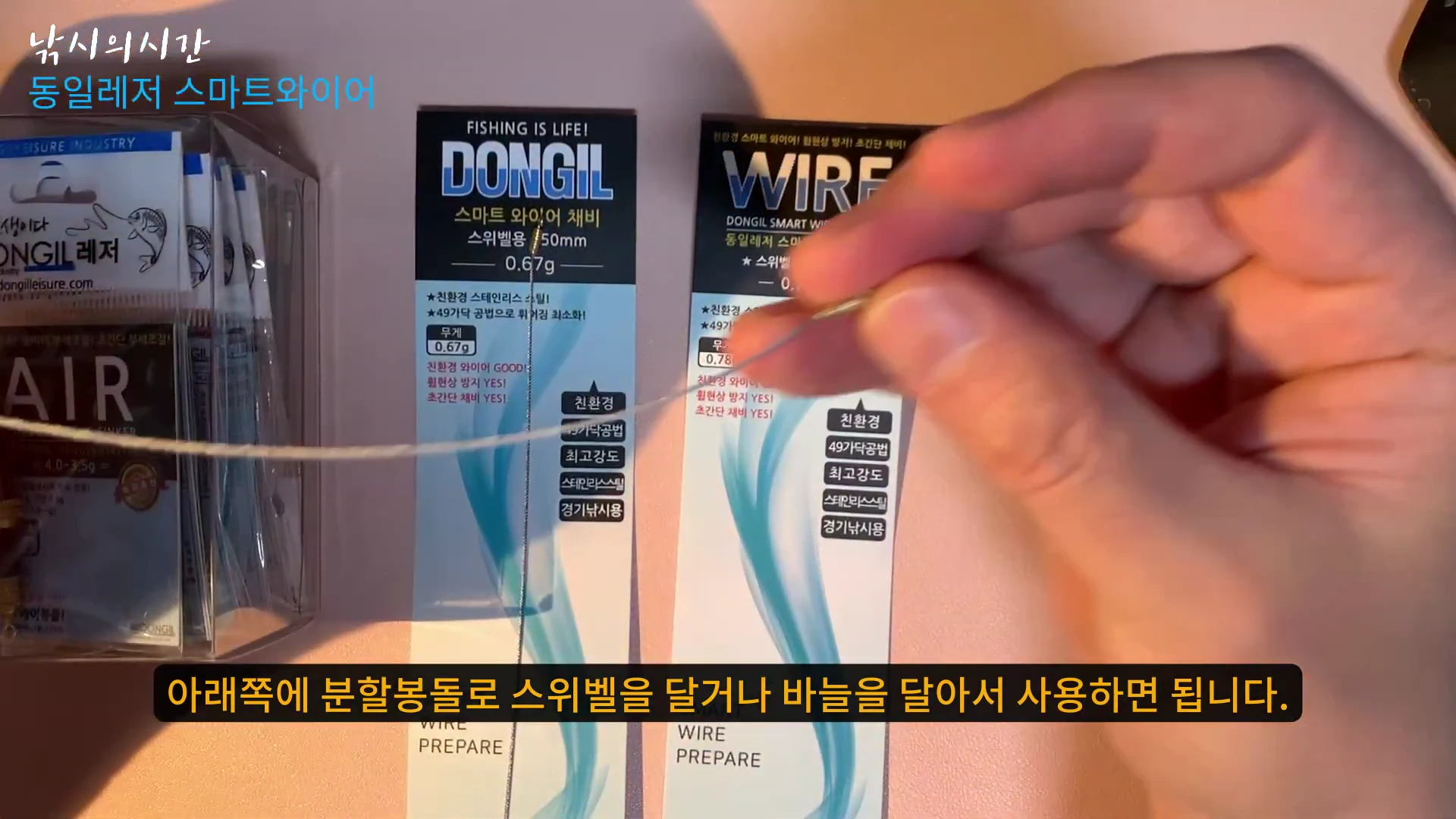 손으로 얇은 와이어 줄을 잡고 펼쳐서 보여주는 모습이며, 뒤편에는 동일레저 스마트 와이어 채비 포장지가 배치되어 있다.