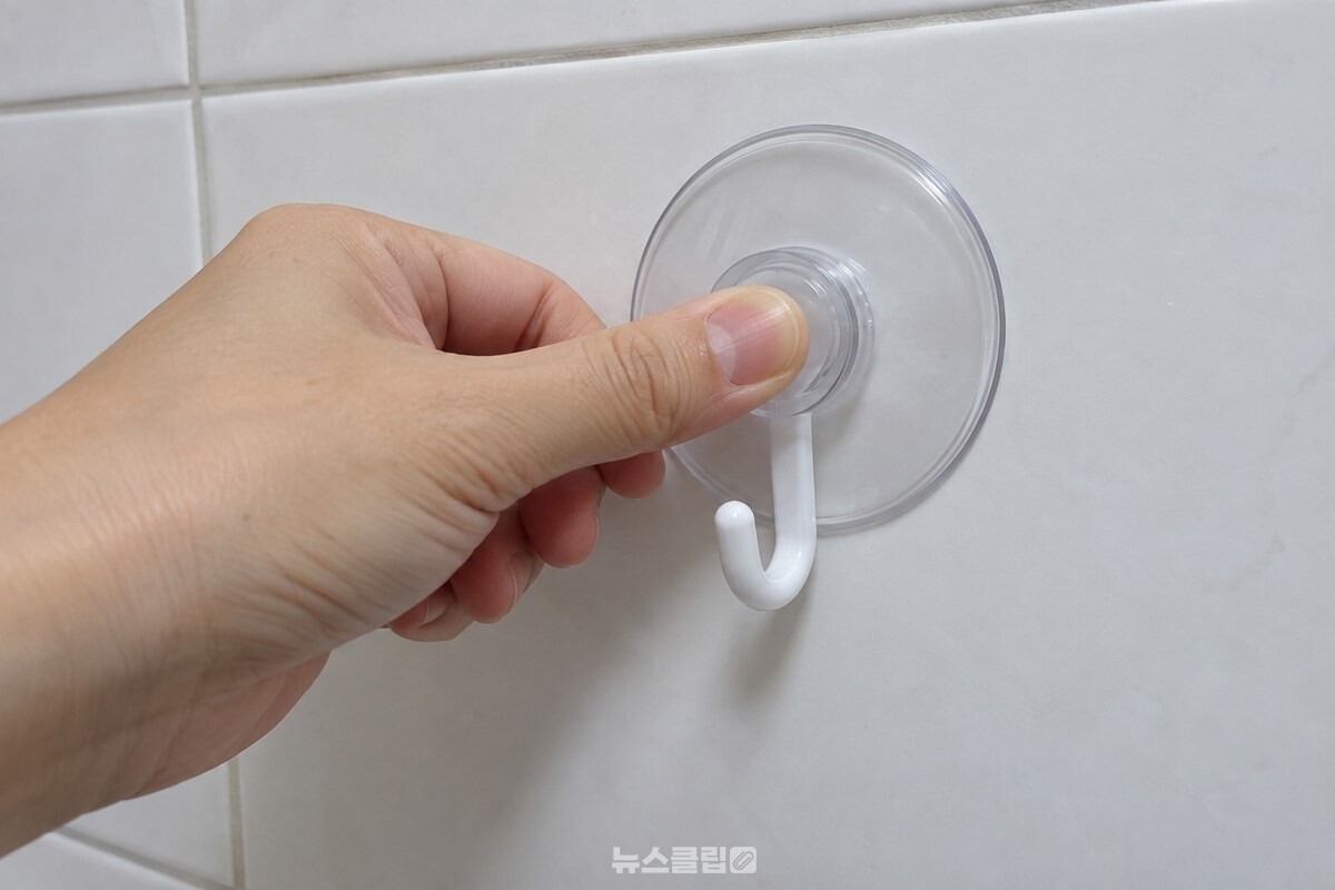 흰 욕실 타일에 붙인 투명 흡착 고리의 고무 테두리를 엄지로 누르는 모습. / 기사 이해를 돕기 위한 생성형 이미지