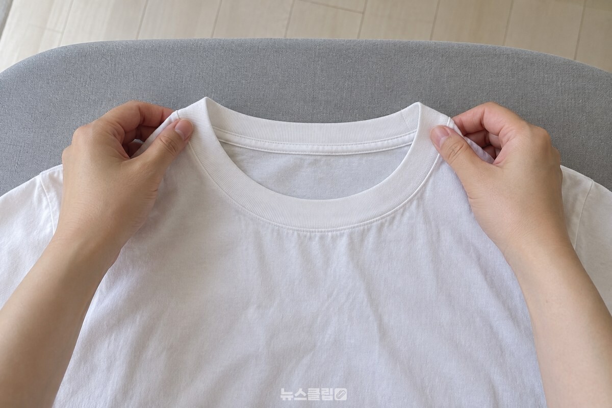 다리미판 위에 펼친 흰 면 티셔츠의 목선을 두 손으로 원래 폭에 맞춰 잡고 있는 모습. / 기사 이해를 돕기 위한 생성형 이미지
