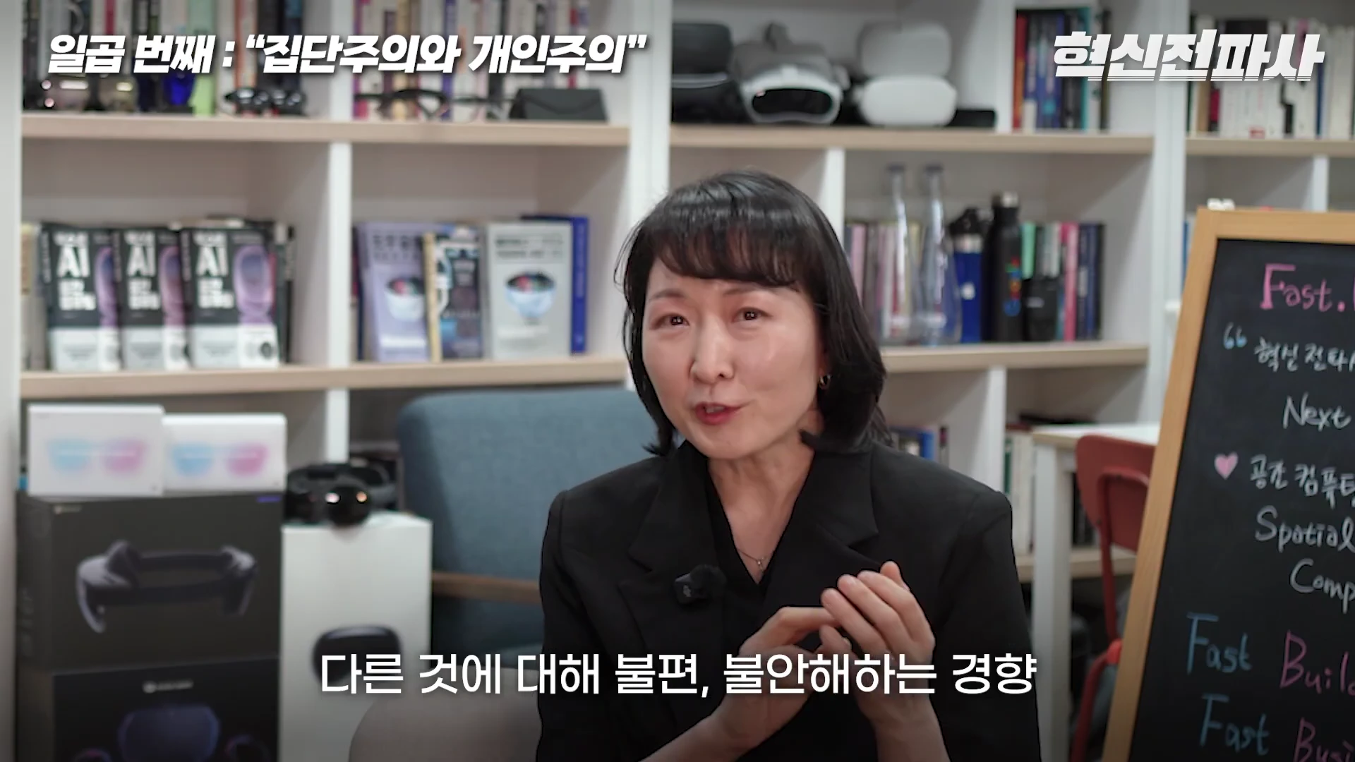 서재를 배경으로 검은색 재킷을 입은 여성이 앉아 대화하고 있으며 화면 상단에는 '일곱 번째: 집단주의와 개인주의'라는 자막이, 하단에는 '다른 것에 대해 불편, 불안해하는 경향'이라는 자막이 배치된 영상 화면.