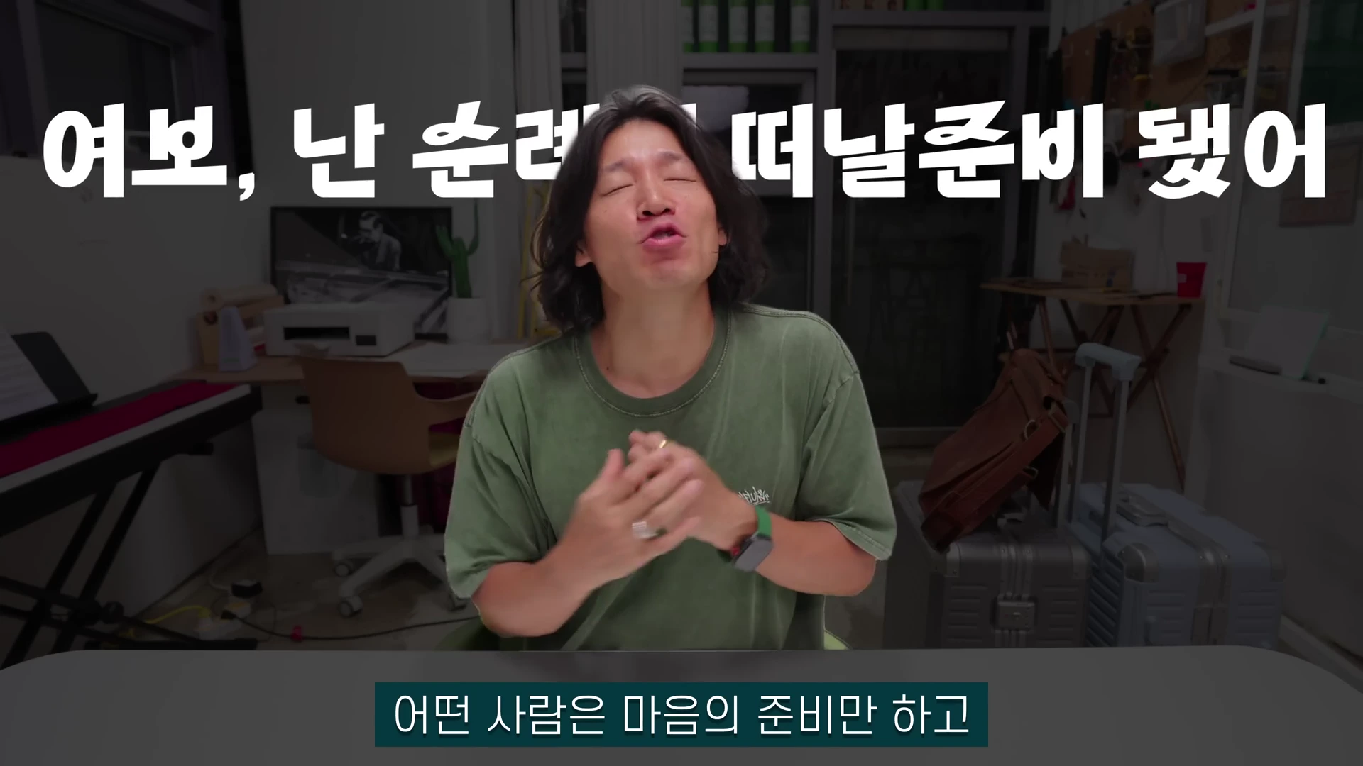 실내에서 초록색 티셔츠를 입은 긴 머리의 남성이 눈을 감고 손을 모은 채 이야기하는 영상 화면. 화면 상단에는 '여보, 난 순례길 떠날 준비 됐어'라는 자막이, 하단에는 '어떤 사람은 마음의 준비만 하고'라는 자막이 있다.