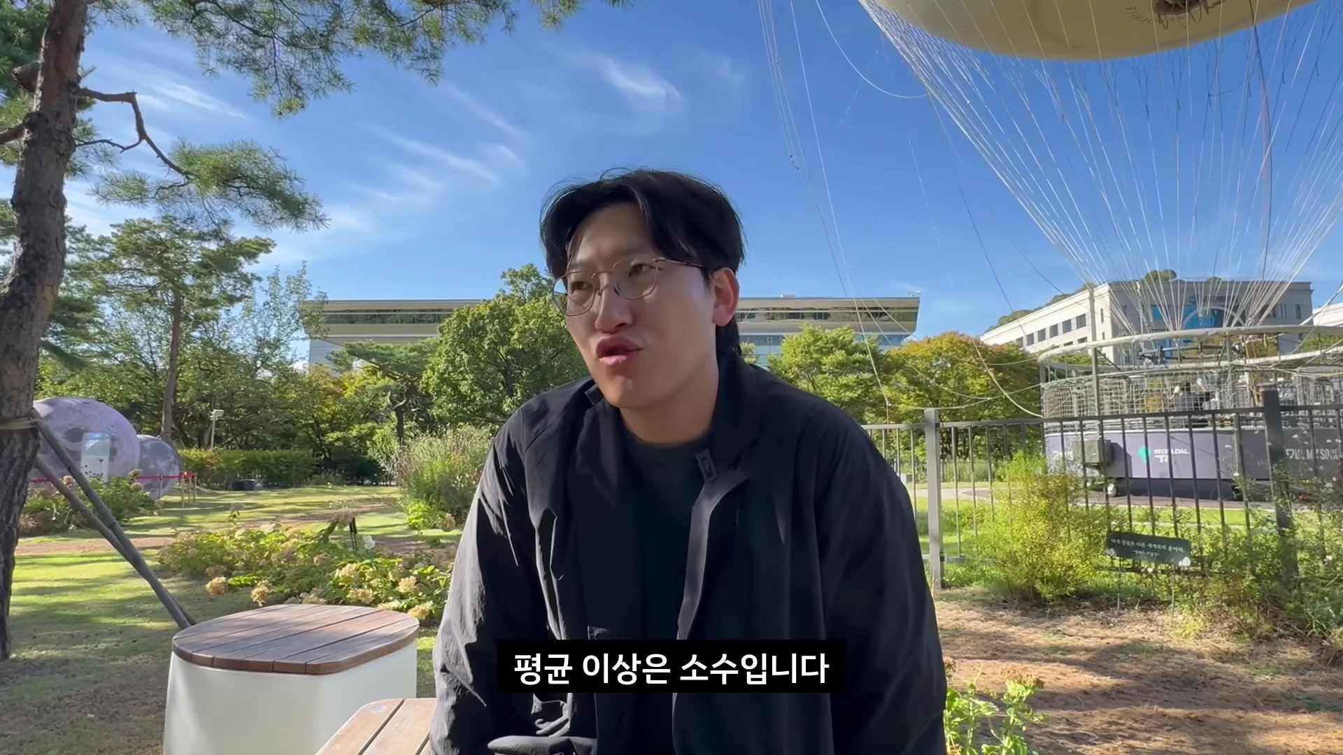 야외 공원에서 안경을 쓴 한 남성이 인터뷰를 진행하고 있으며 화면 하단에는 '평균 이상은 소수입니다'라는 자막이 표시되어 있습니다.