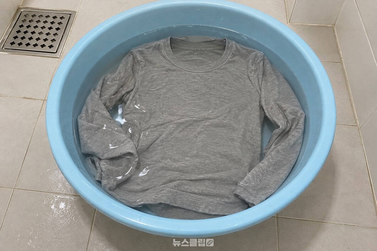 깨끗한 욕실 바닥의 대야 안에 미지근한 린스 물과 줄어든 긴팔 티셔츠가 펼쳐져 있다. / 기사 이해를 돕기 위한 생성형 이미지