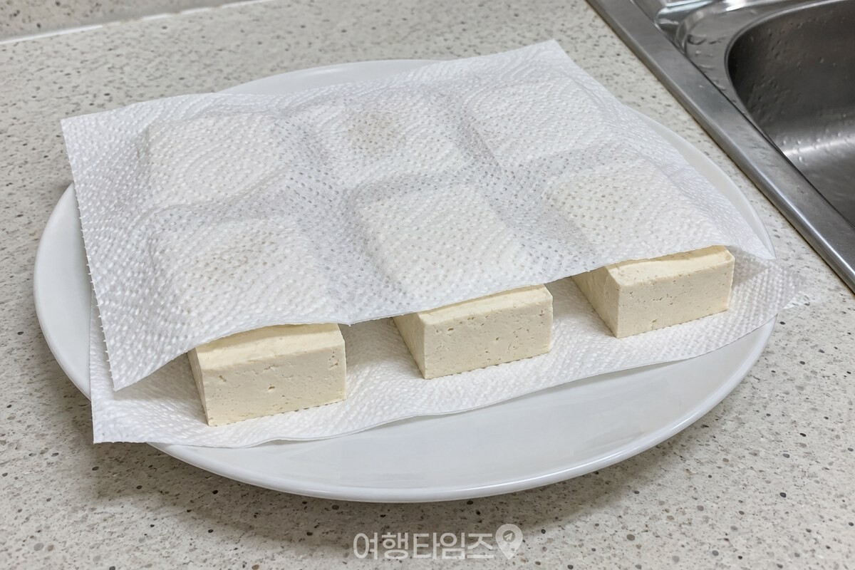 키친타월 위에 1.5cm 두께로 썬 단단한 두부를 올리고 위를 덮어 물기를 빼는 모습. / 기사 이해를 돕기 위한 생성형 이미지