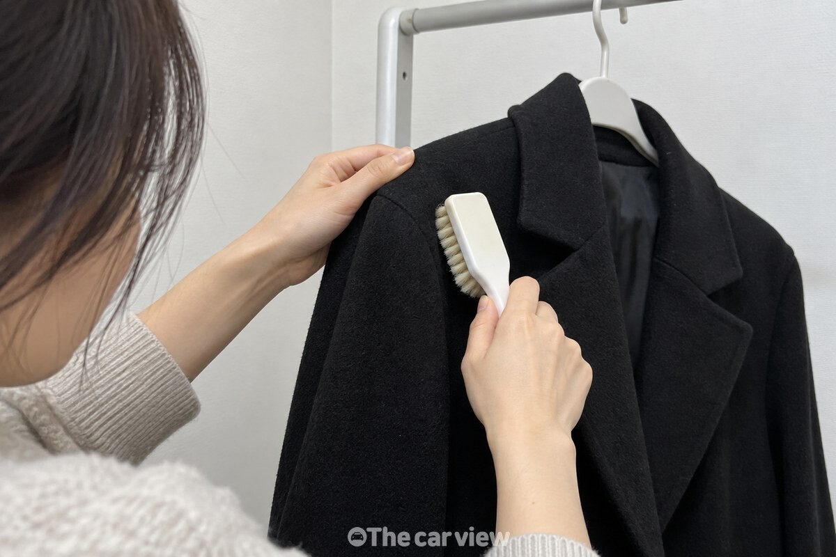 옷걸이에 건 검은 모직 코트의 어깨 부분을 운동화 세척 솔로 아래로 빗는 모습. / 기사 이해를 돕기 위한 생성형 이미지