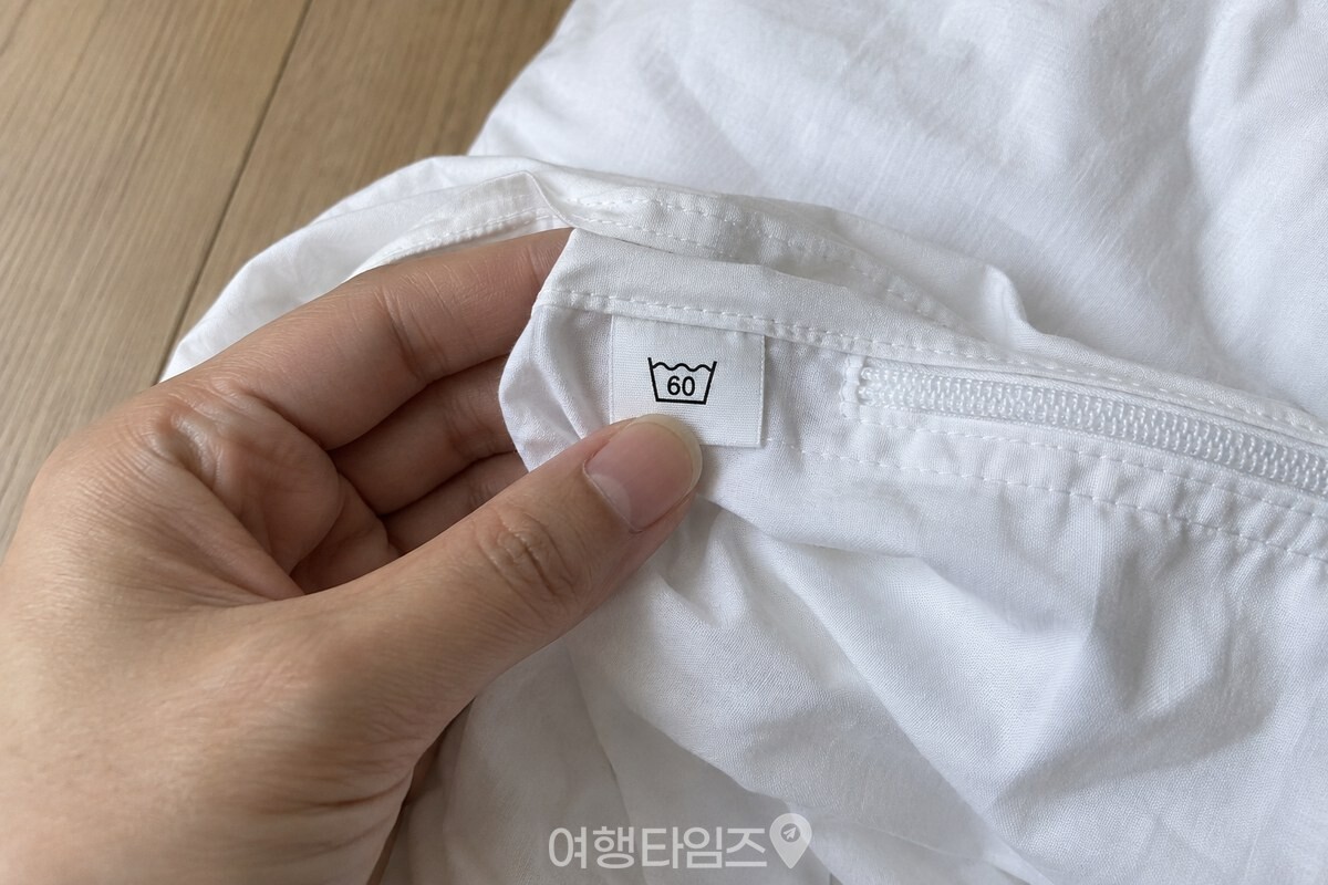 이불 커버 안쪽 세탁 라벨의 60도 물세탁 표시를 손가락으로 확인하고 있다. / 기사 이해를 돕기 위한 생성형 이미지
