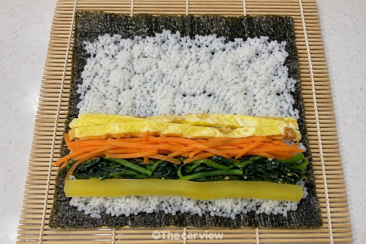 김 위에 밥과 속재료를 고르게 올려 김발 위에 펼쳐 둔 김밥 재료. / 기사 이해를 돕기 위한 생성형 이미지
