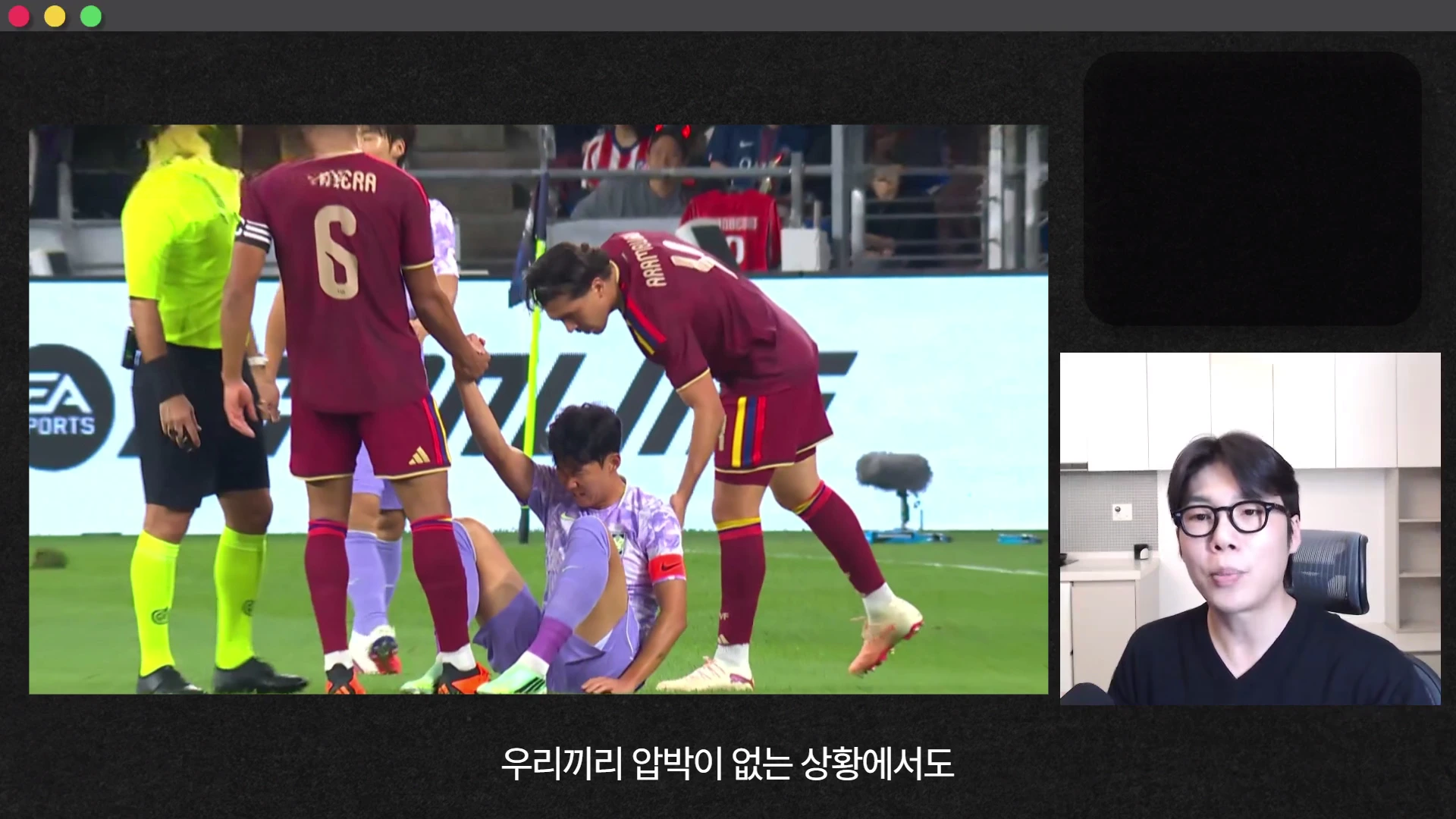 축구 경기장에서 한 선수가 넘어져 있고 상대 팀 선수들이 그를 일으켜 세우려는 모습이 담긴 영상 화면과, 그 옆에서 안경을 쓴 남성이 이야기를 나누는 모습이 함께 나타나 있습니다.