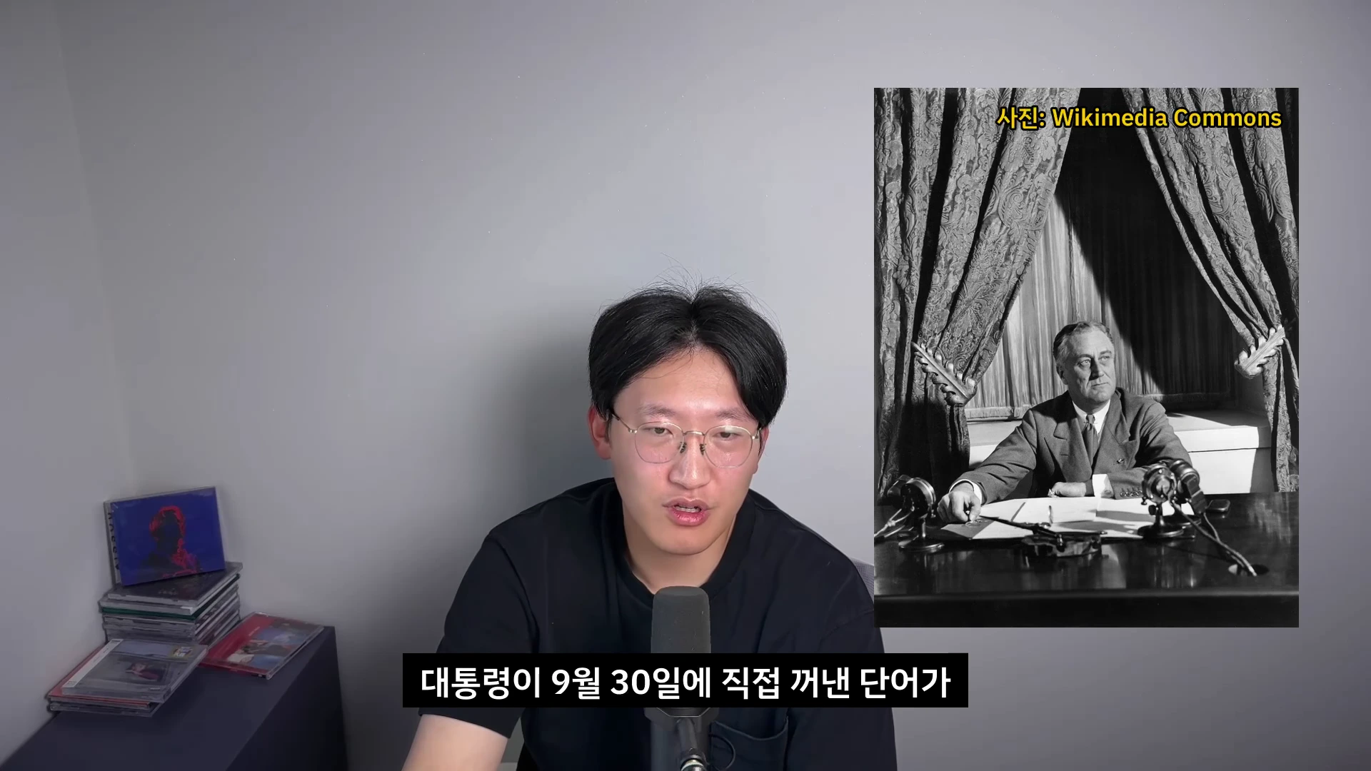 안경을 쓴 남성이 마이크 앞에 앉아 말하고 있고, 화면 오른쪽에는 프랭클린 D. 루즈벨트 대통령이 라디오 방송을 하는 흑백 사진이 자료 화면으로 삽입되어 있다.