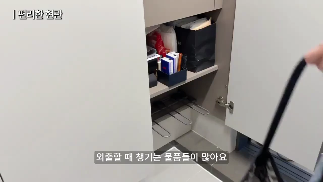 열려 있는 신발장 안에 향수, 빗, 가방 등 외출용 소품들이 정리되어 있고 한쪽 문은 사람이 손으로 열고 있는 모습