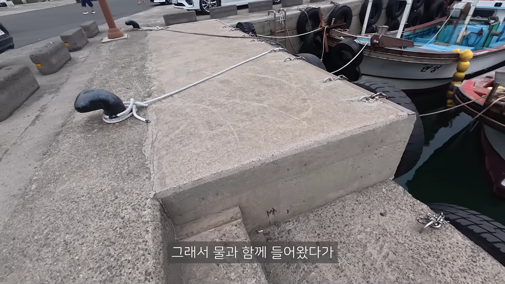콘크리트로 만들어진 항구 선착장 가장자리와 그 옆에 정박 중인 작은 배들이 보이는 모습