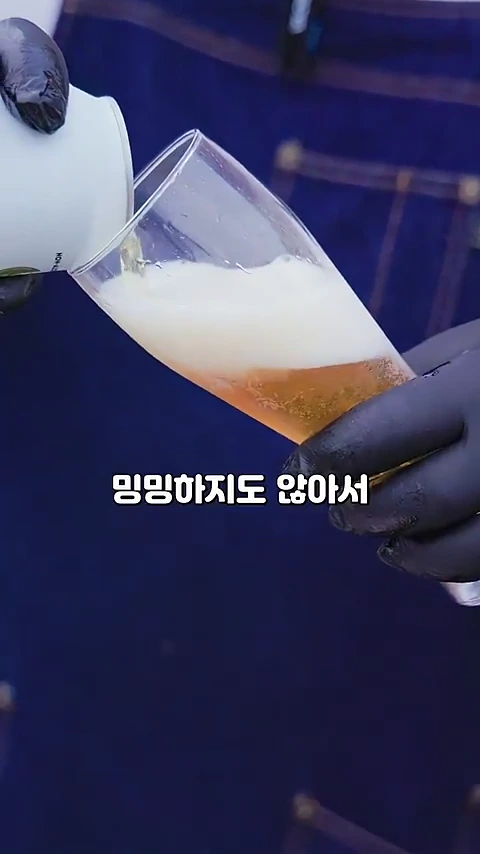 검은색 라텍스 장갑을 낀 손이 흰색 캔 맥주를 들고 유리잔에 맥주를 따르고 있으며, 화면 중앙에는 '밍밍하지도 않아서'라는 자막이 배치되어 있습니다.
