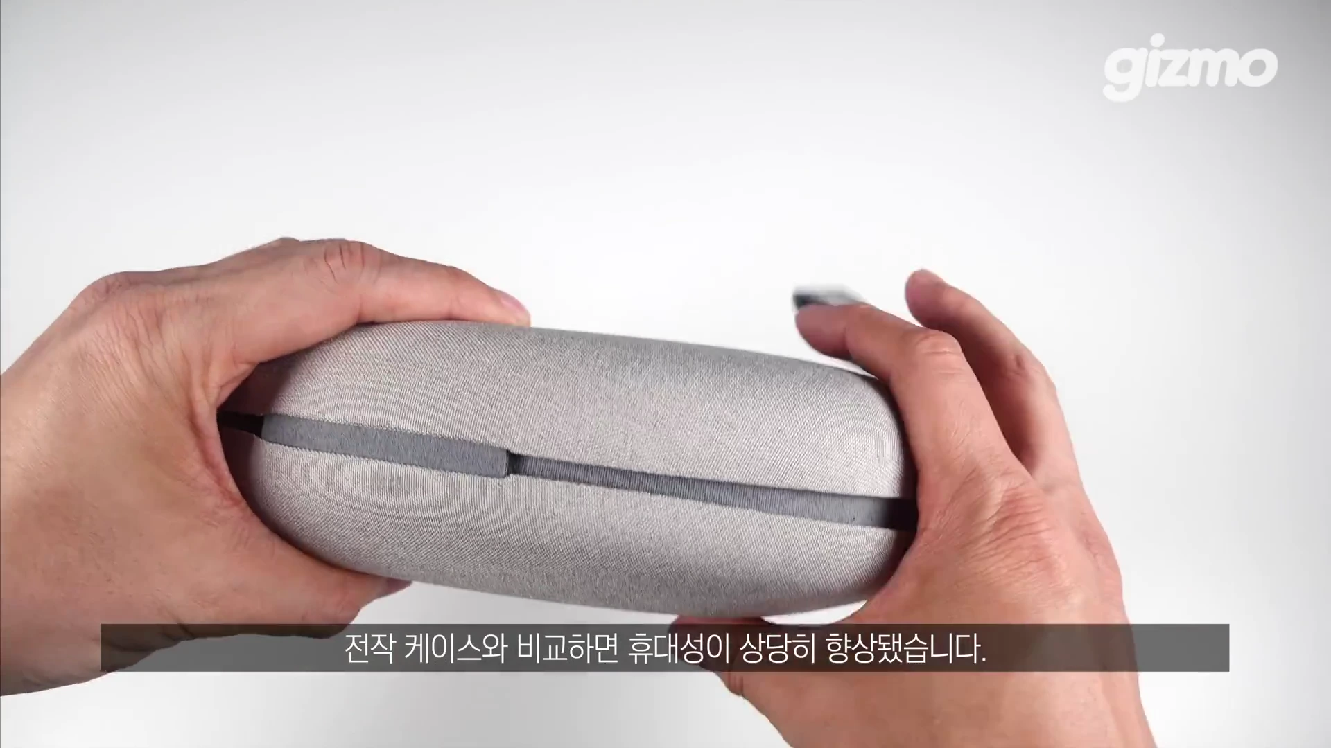 두 손으로 밝은 회색의 타원형 헤드폰 전용 케이스를 들고 있는 모습.