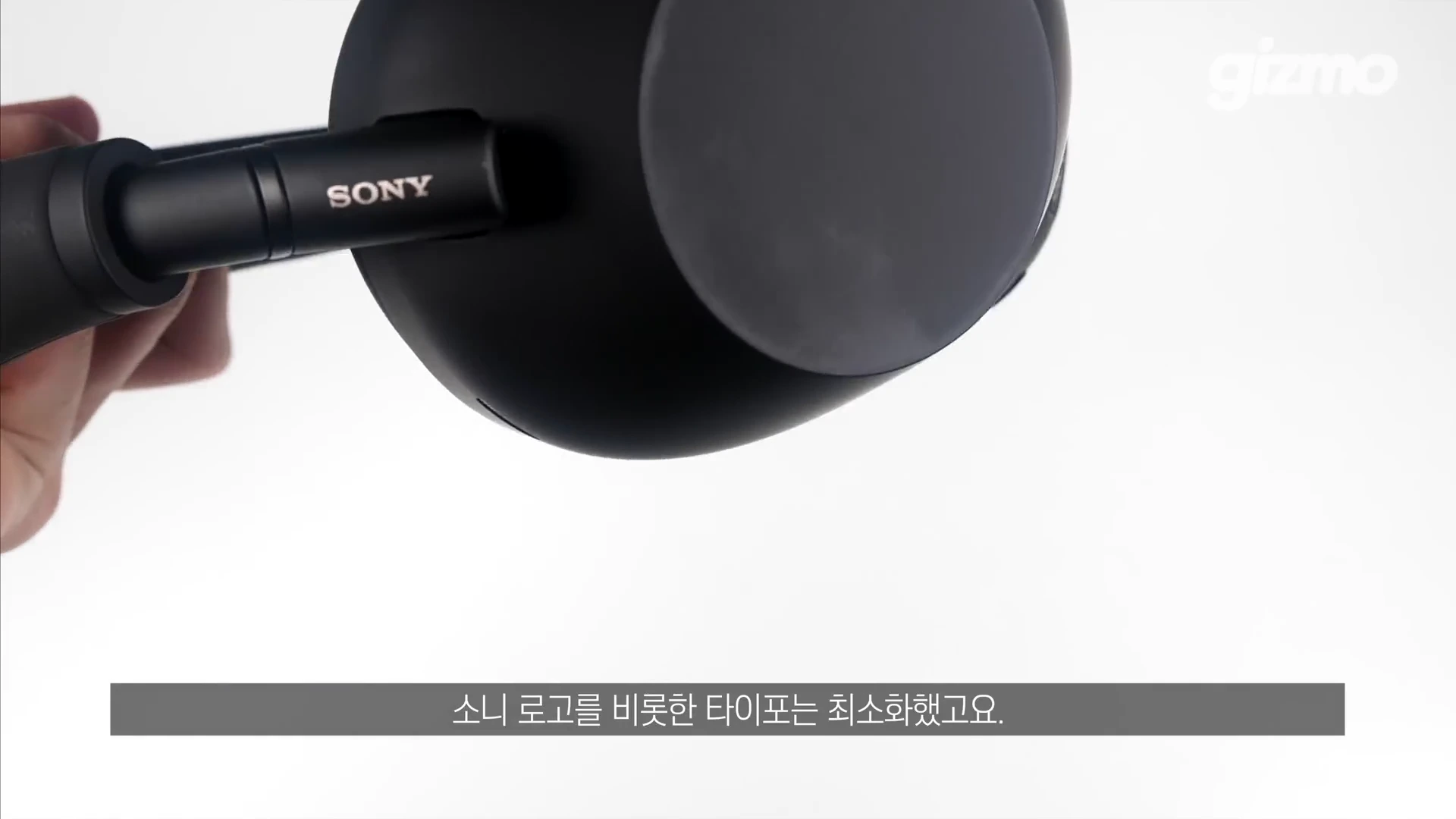 검은색 무선 헤드폰의 이어컵 측면에 새겨진 작은 소니 로고를 손으로 들고 있는 모습.