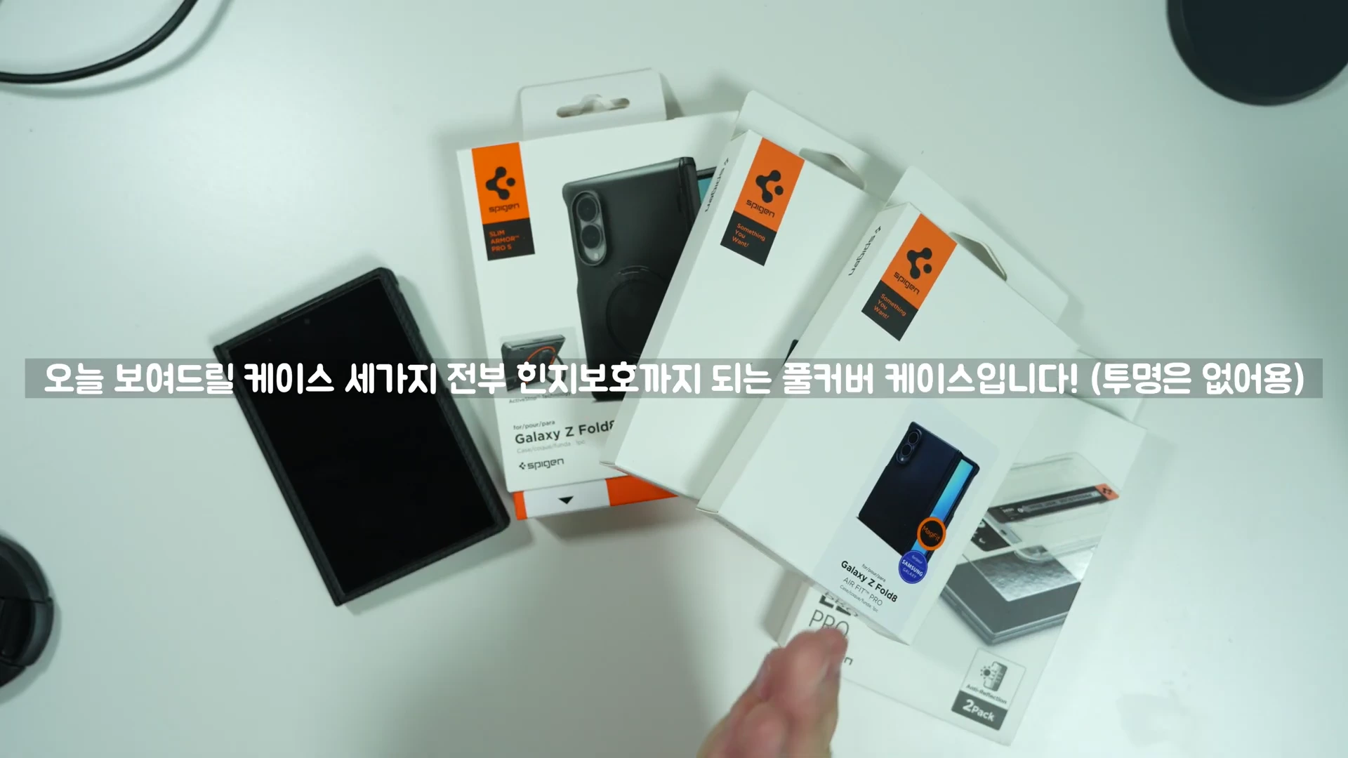 스마트폰 케이스 패키지 3개와 케이스가 장착된 폴더블 스마트폰이 하얀 테이블 위에 놓여 있으며, 화면 중앙에 '오늘 보여드릴 케이스 세가지 전부 힌지보호까지 되는 풀커버 케이스입니다! (투명은 없어용)'라는 자막이 표시되어 있습니다.