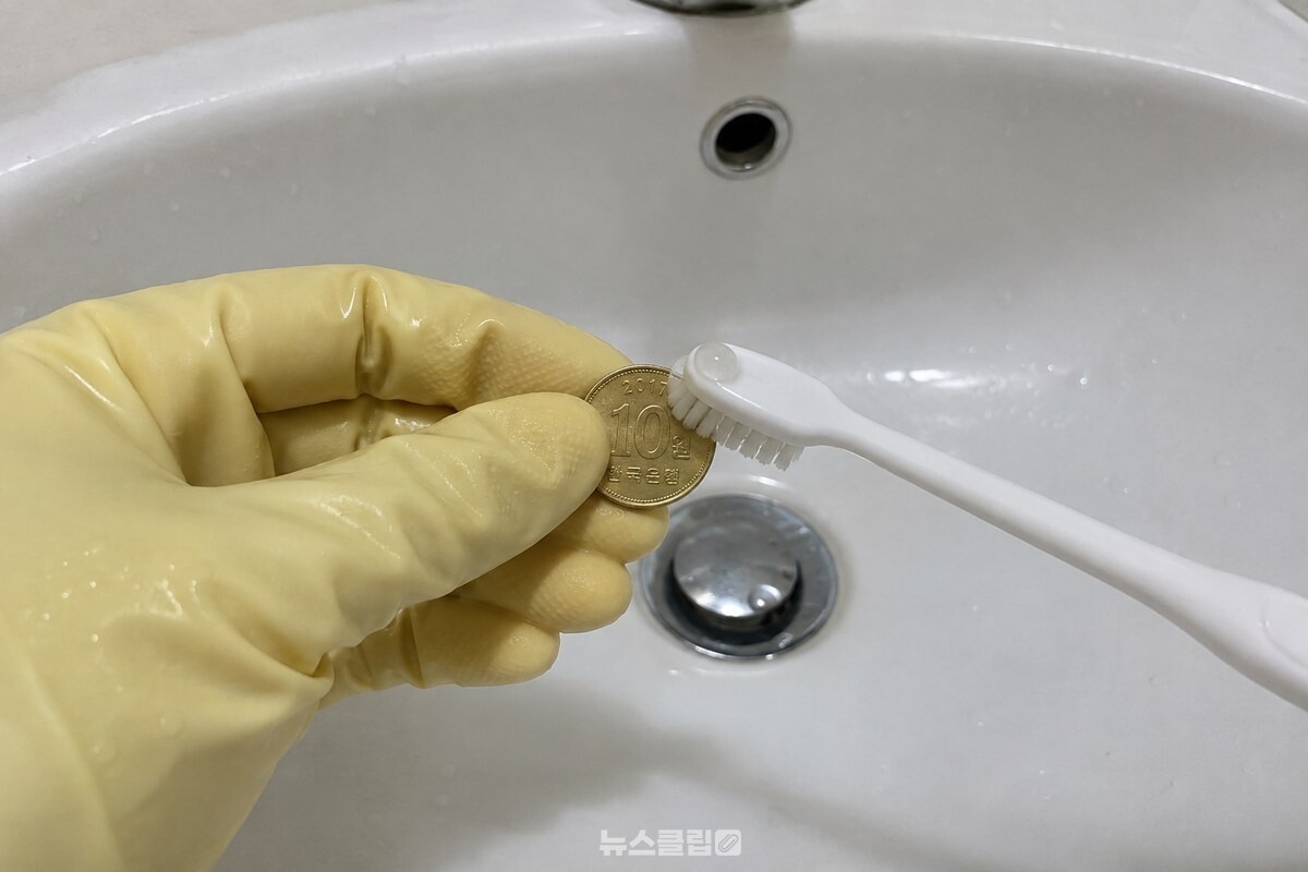 고무장갑을 낀 손이 칫솔로 십원짜리 동전의 한쪽 면을 닦고 있다. / 기사 이해를 돕기 위한 생성형 이미지