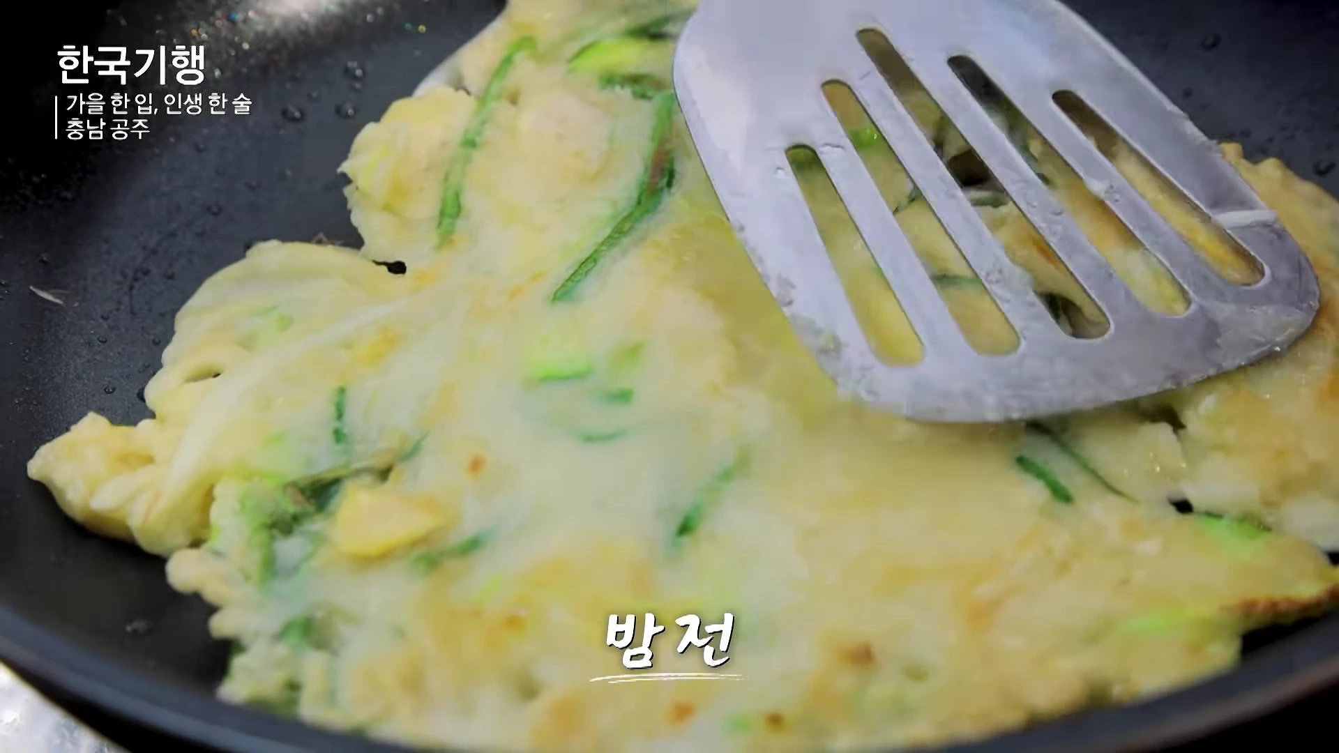 프라이팬 위에서 조리 중인 노릇하고 얇은 밤전과 이를 뒤집는 뒤집개 모습.
