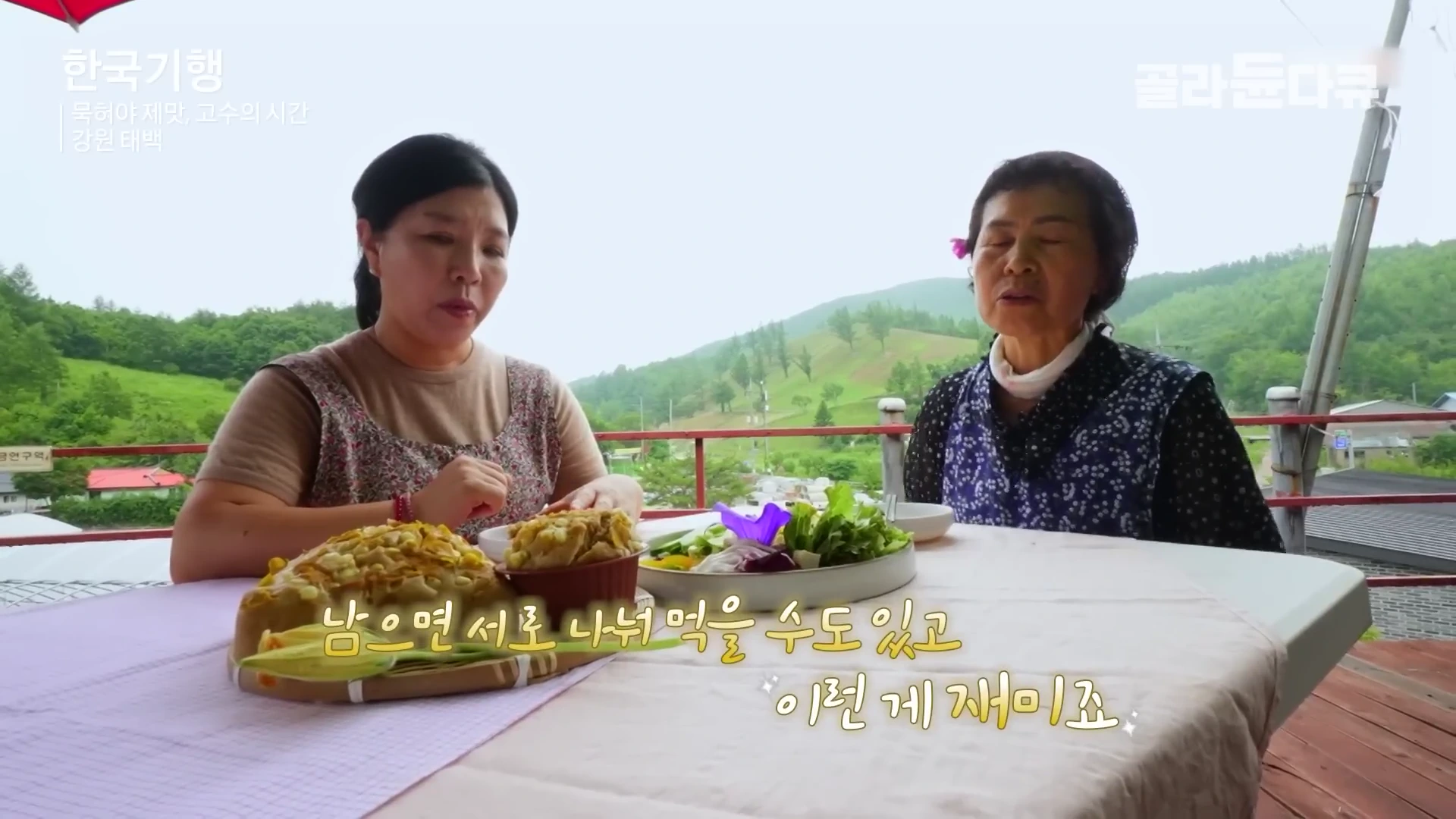야외 테이블에 나란히 앉은 중년 여성과 노년 여성이 순두부 요리를 앞에 두고 대화를 나누고 있다.