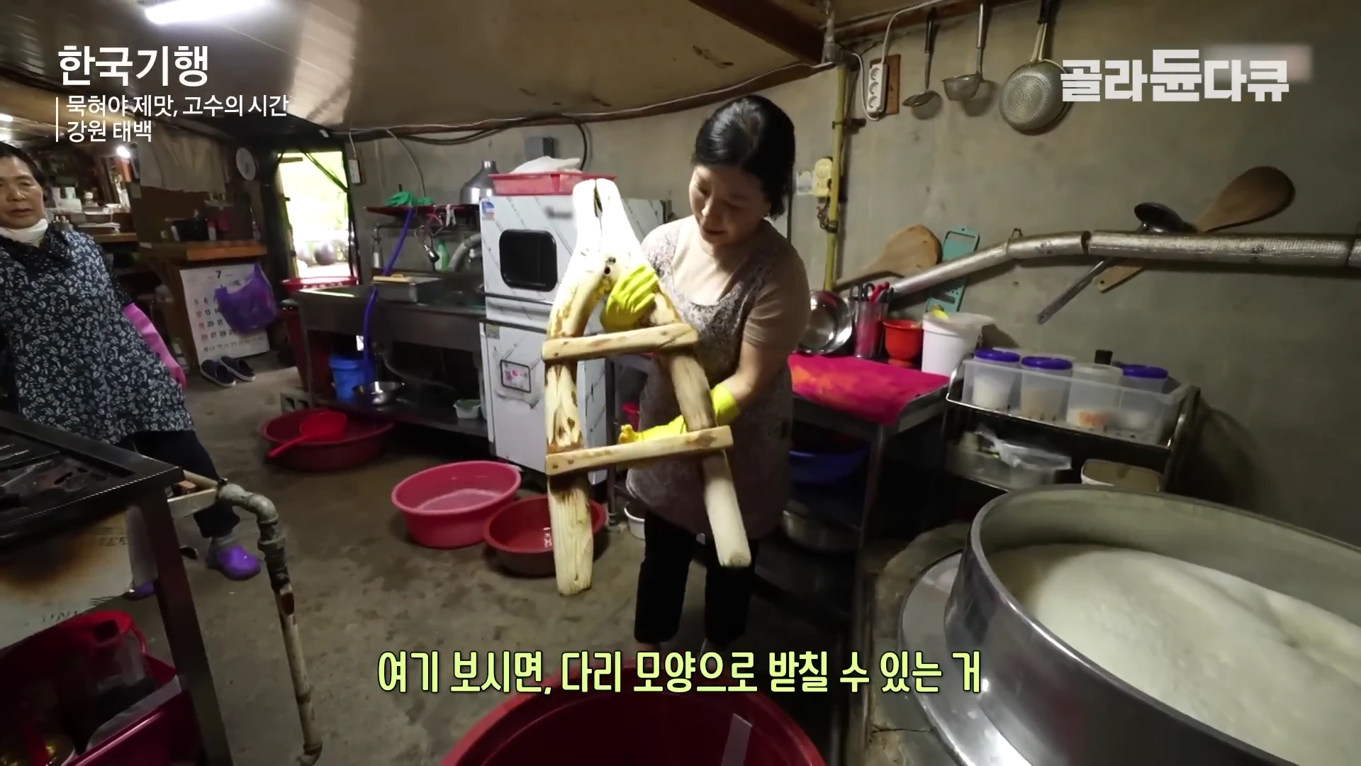 두 명의 여성이 시골의 오래된 부엌에서 두부를 만들 때 사용하는 낡은 나무 도구를 들어 보이고 있다.