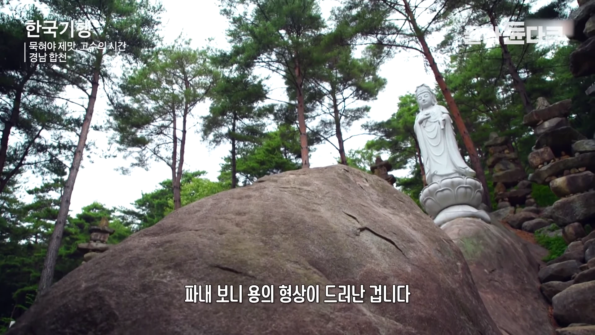 경남 합천 허굴산의 울창한 숲속, 거대한 자연 암석 위에 세워진 흰색 관세음보살 불상과 그 아래 돌탑들이 보입니다.