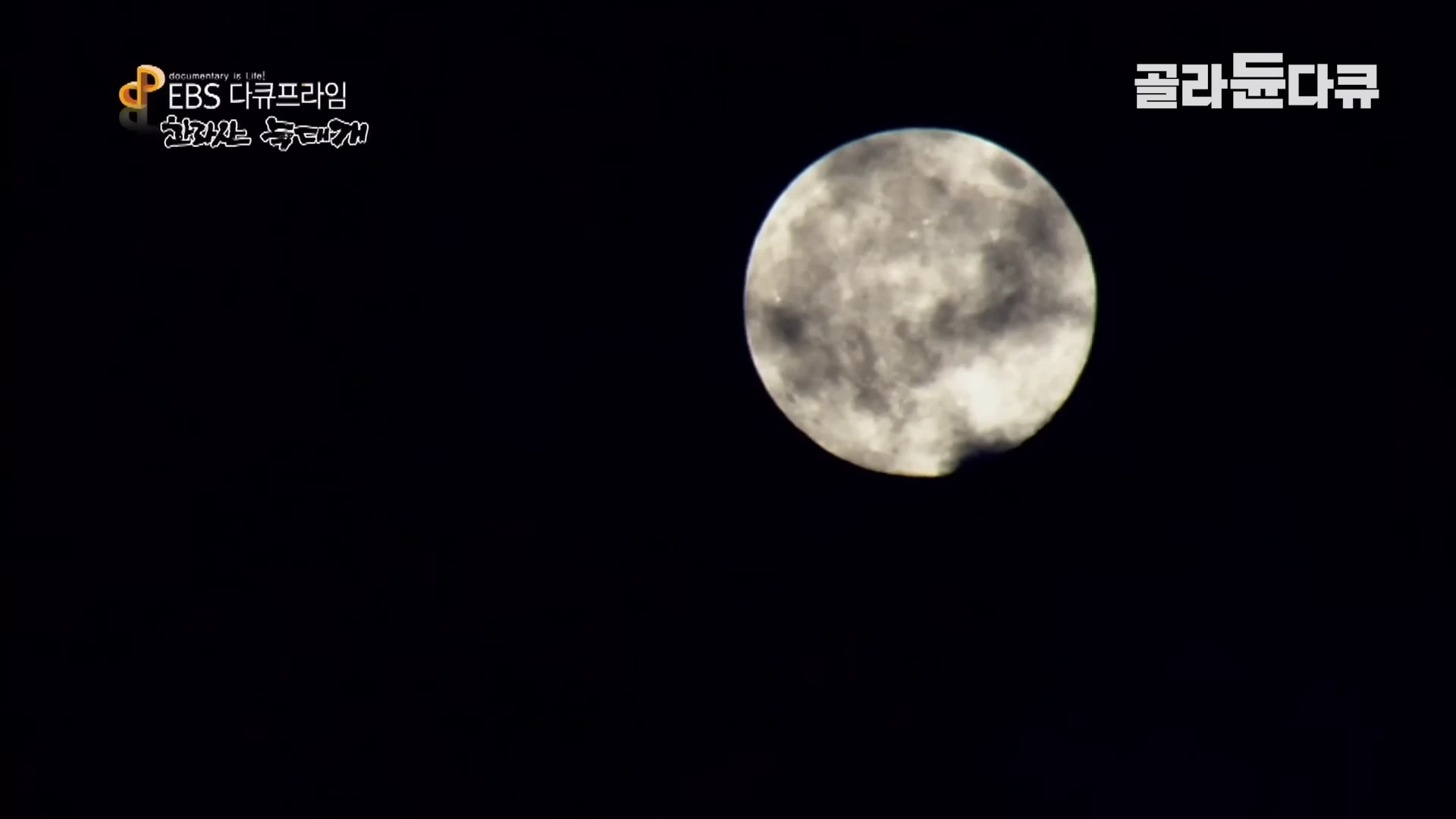 검은 밤하늘에 구름이 살짝 걸쳐 있는 밝고 둥근 보름달이 떠 있다.