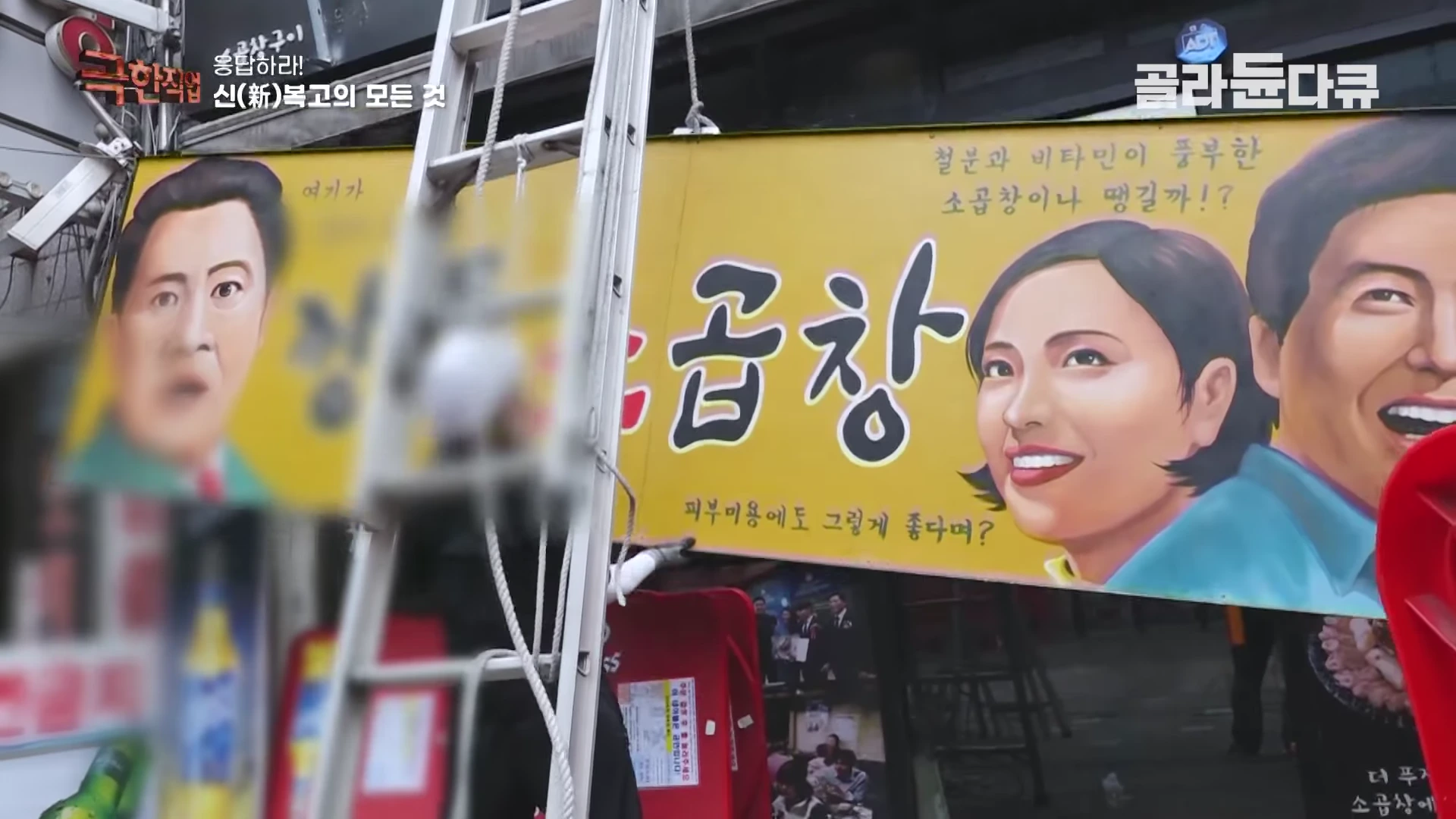 사람들이 사다리에 올라타 80년대 스타일의 인물화가 그려진 노란색 식당 간판을 건물 외벽에 설치하고 있다.