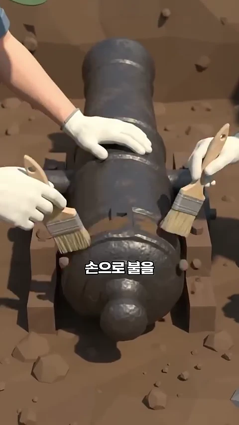 흙 속에 묻혀 있는 둥근 통 모양의 옛 화포 유물을 작업자들이 작은 붓으로 조심스럽게 털어내고 있는 모습입니다.
