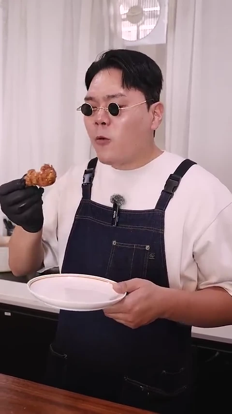 선글라스를 쓴 남성이 검은색 위생 장갑을 끼고 갓 튀긴 치킨 한 조각을 들어 올리며 시식하는 모습