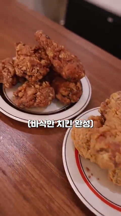 두 접시에 담긴 노릇하게 튀겨진 치킨 조각들이 나무 테이블 위에 놓여 있고, 화면 중앙에는 바삭한 치킨 완성이라는 흰색 자막이 표시되어 있습니다.