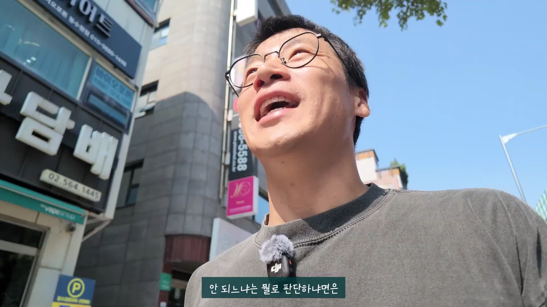 안경을 쓴 남성이 야외 거리에서 하늘을 올려다보며 무언가를 설명하는 모습이 담긴 셀카 구도의 영상 캡처 화면