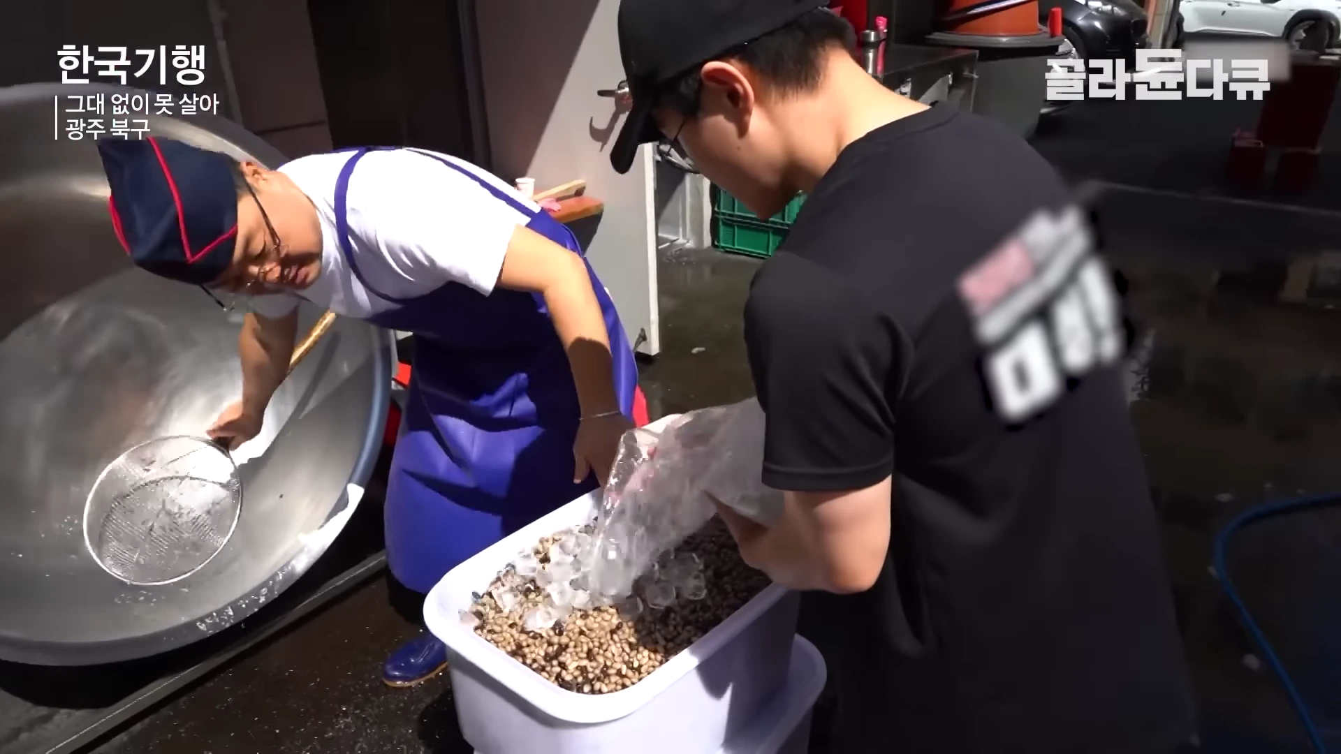 두 사람이 야외에서 큰 솥과 플라스틱 통에 콩을 다루며 작업하는 모습