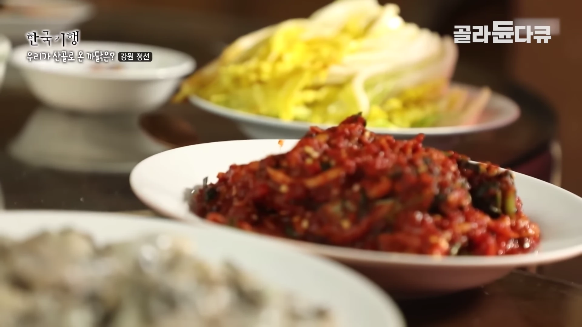 흰 접시에 담긴 빨간 양념의 김치와 쌈 채소가 놓인 식탁의 모습