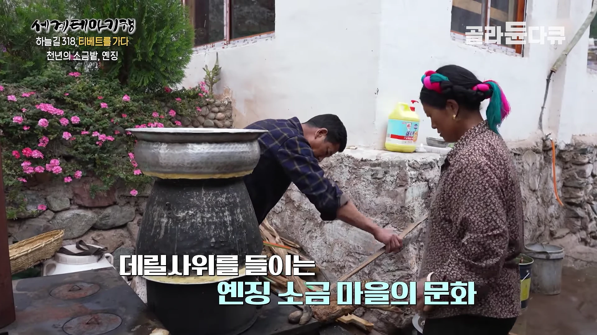 실내에서 전통적인 방식으로 솥을 사용해 술을 빚고 있는 남성과 그 옆에 서 있는 여성이 보입니다.