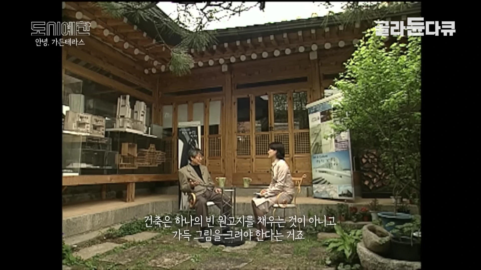 한옥 마당에 앉아 인터뷰를 나누고 있는 남성과 여성, 주변에는 건축 모형들이 전시되어 있다.