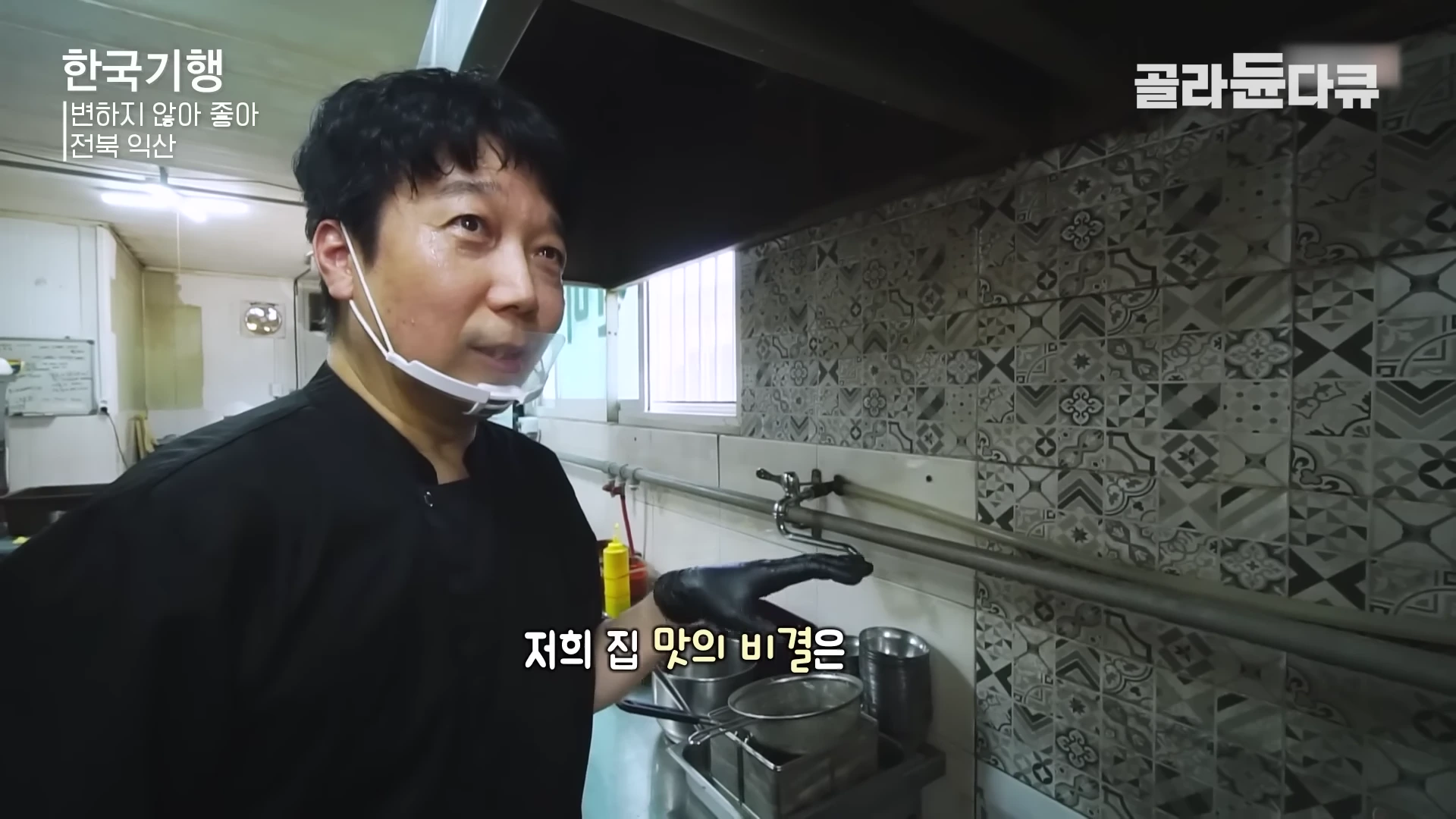주방에서 검은색 위생 장갑을 낀 식당 주인이 손으로 가리키며 이야기를 하고 있는 모습
