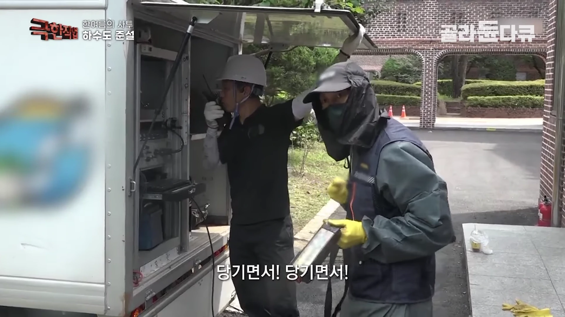 작업복을 입고 장갑을 낀 두 명의 작업자가 하수도 준설차 옆에서 무전기를 사용하며 작업을 지휘하고 있는 모습.