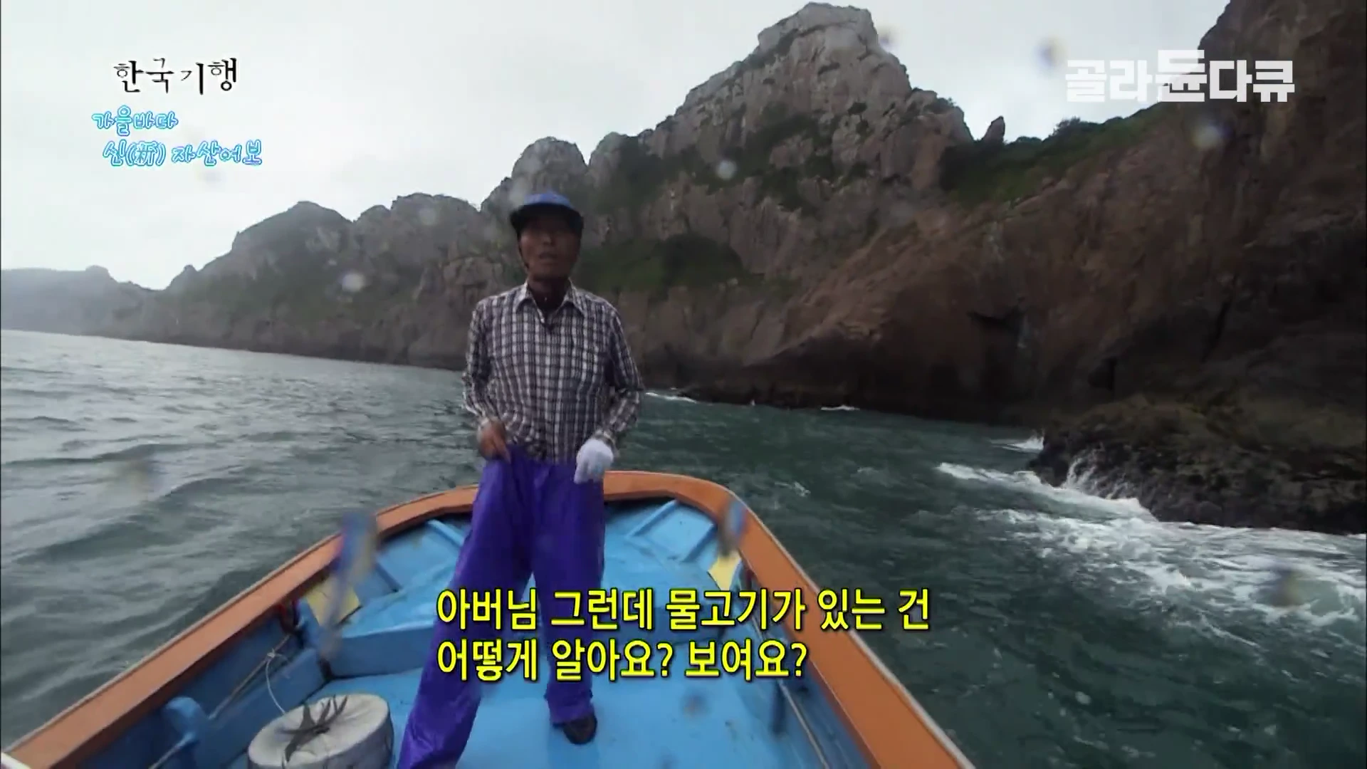 바다 위 작은 어선에 서 있는 낚시꾼 뒤로 높고 험준한 바위 절벽이 펼쳐져 있으며, 화면 하단에는 물고기의 위치를 어떻게 아는지 묻는 자막이 표시되어 있다.