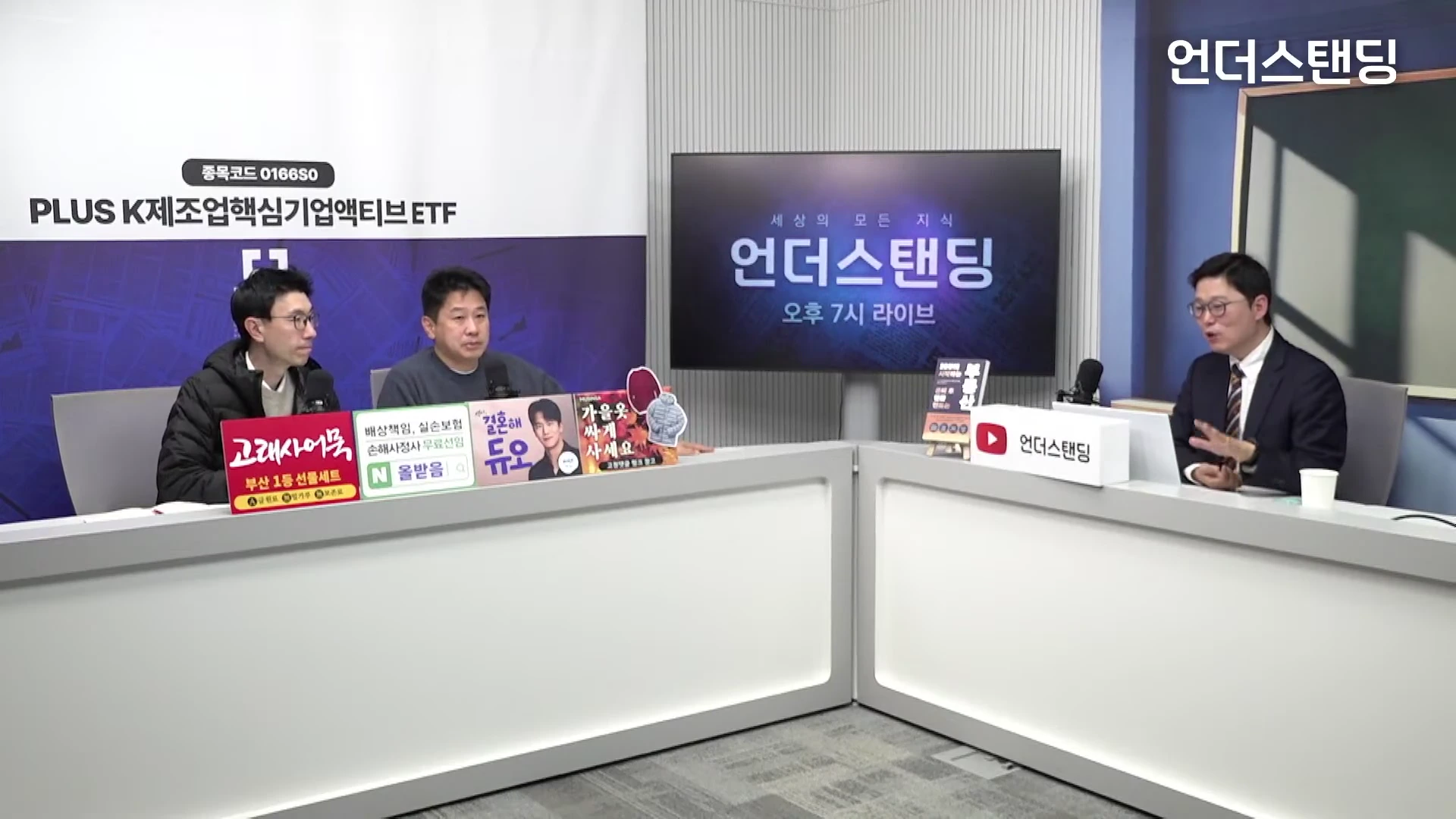 밝은 스튜디오에서 세 명의 남성이 책상을 사이에 두고 앉아 대화를 나누고 있다.