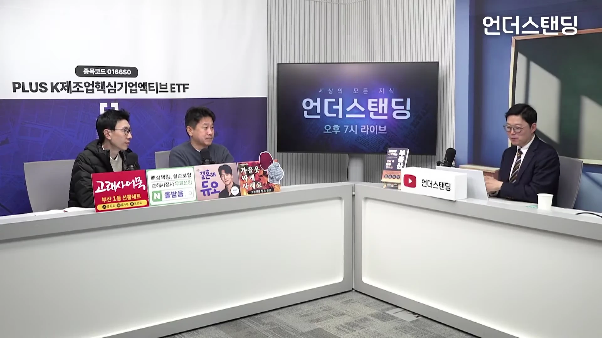 두 명의 출연자가 데스크에 앉아 진행자와 대화를 나누는 스튜디오 토크쇼 장면입니다.
