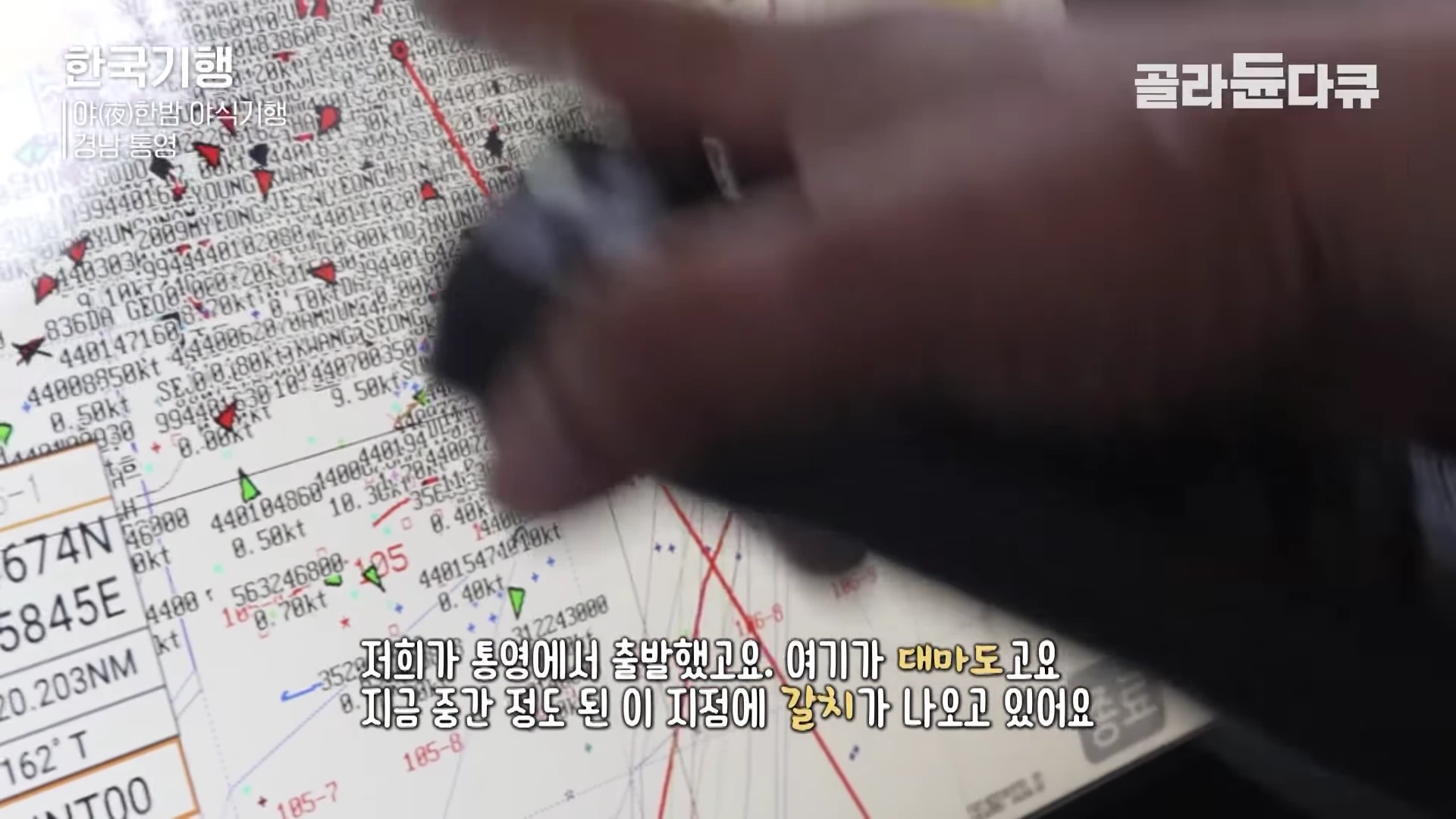 배의 조타실에 설치된 내비게이션 화면 위로 사람의 손가락이 특정 위치를 가리키고 있다.