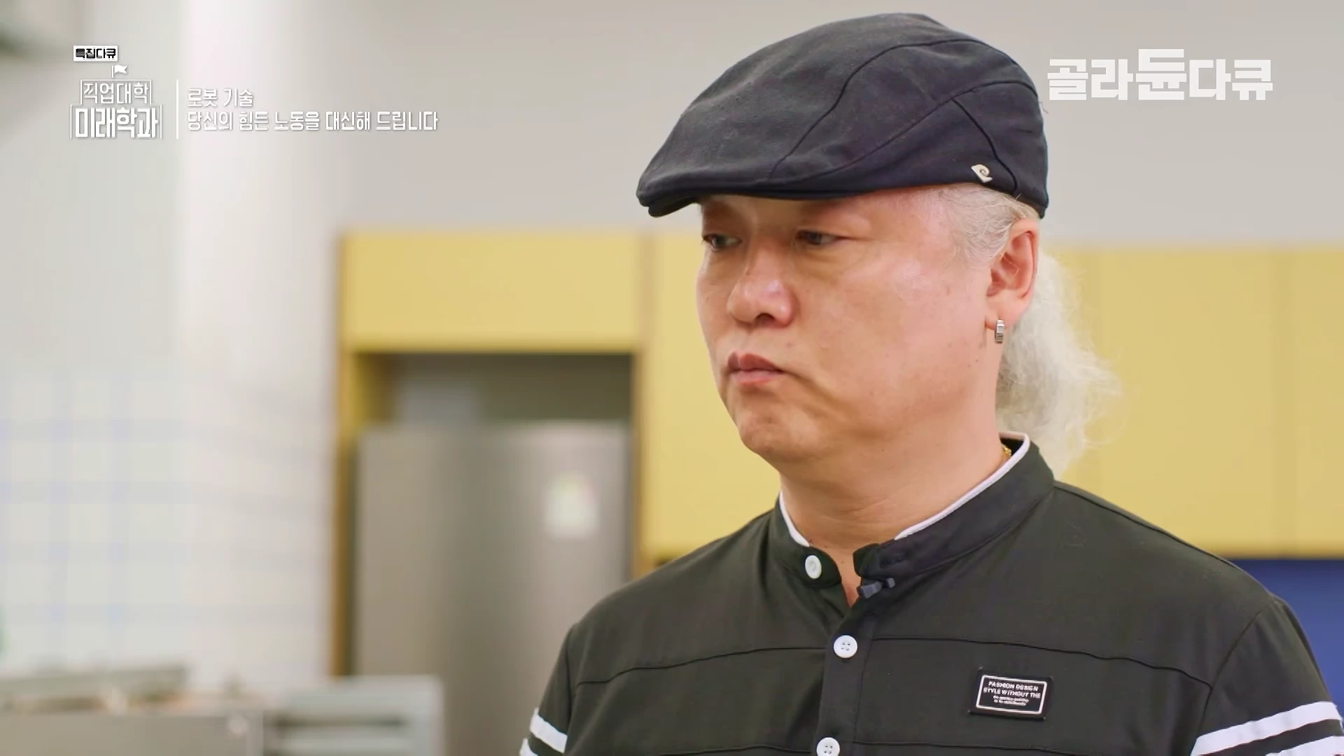 실내에서 검은색 모자와 검은색 상의를 입은 중년 남성이 진지한 표정으로 인터뷰에 응하고 있는 모습이다.